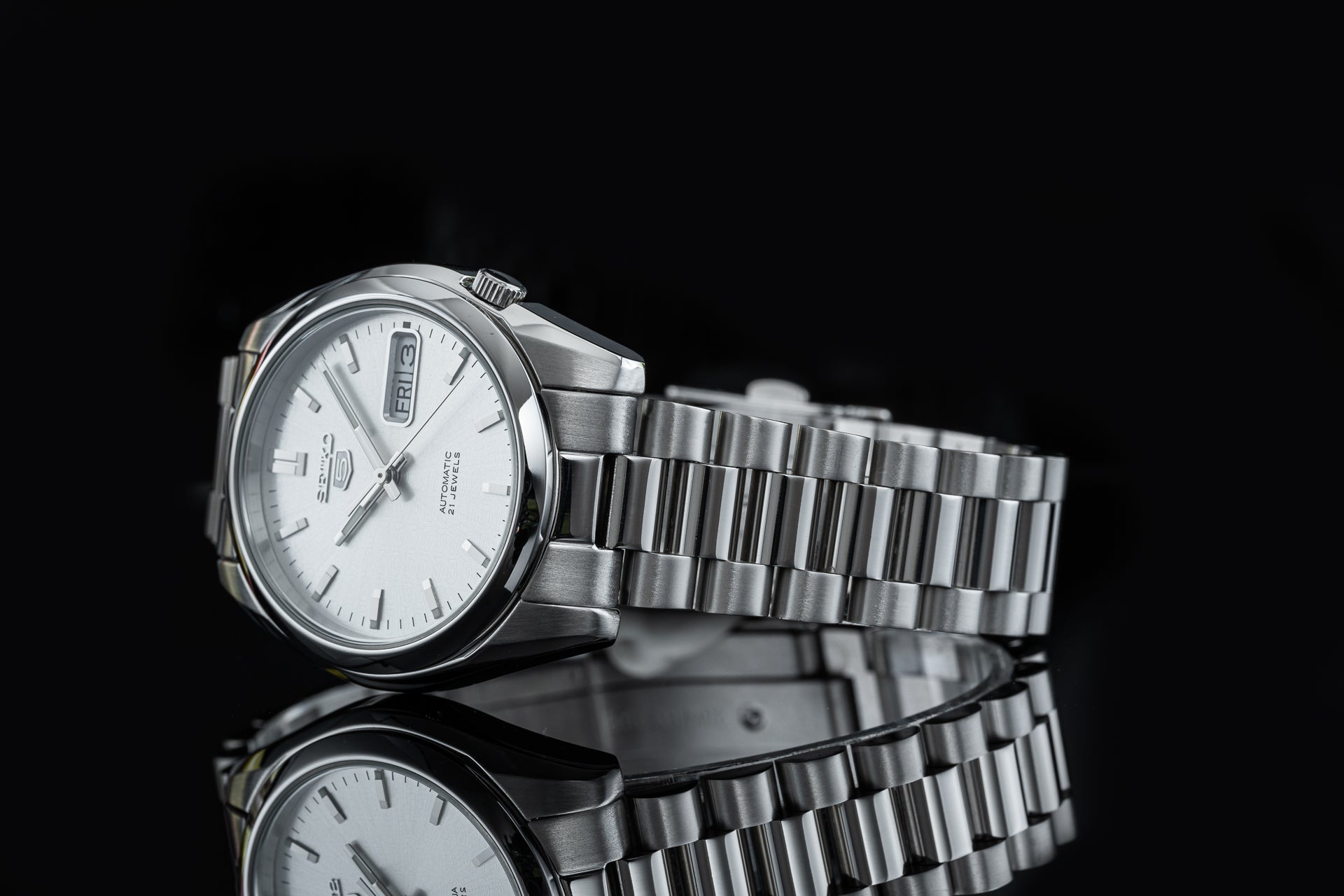 Seiko 5 SNKL automatic stainless steel watch with white dial, day-date window, and matching metal bracelet on black background