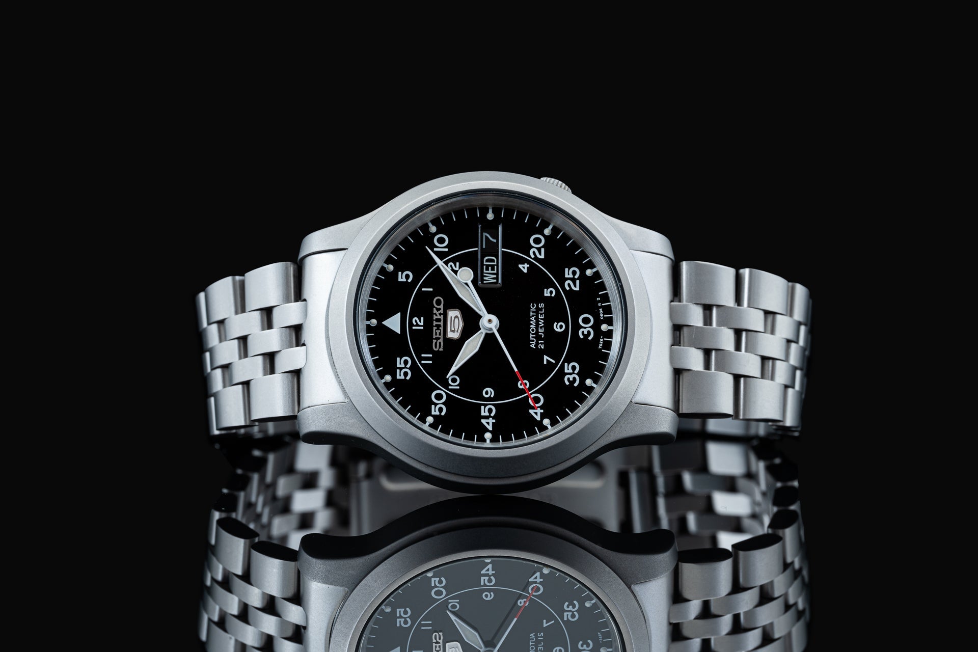 Seiko SNK809 automatic watch with stainless steel bracelet, black dial, day-date window, and Arabic numerals on black background