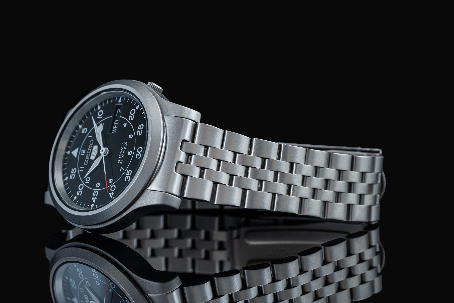 Seiko SNK807 stainless steel automatic watch with black dial and metal bracelet on black background