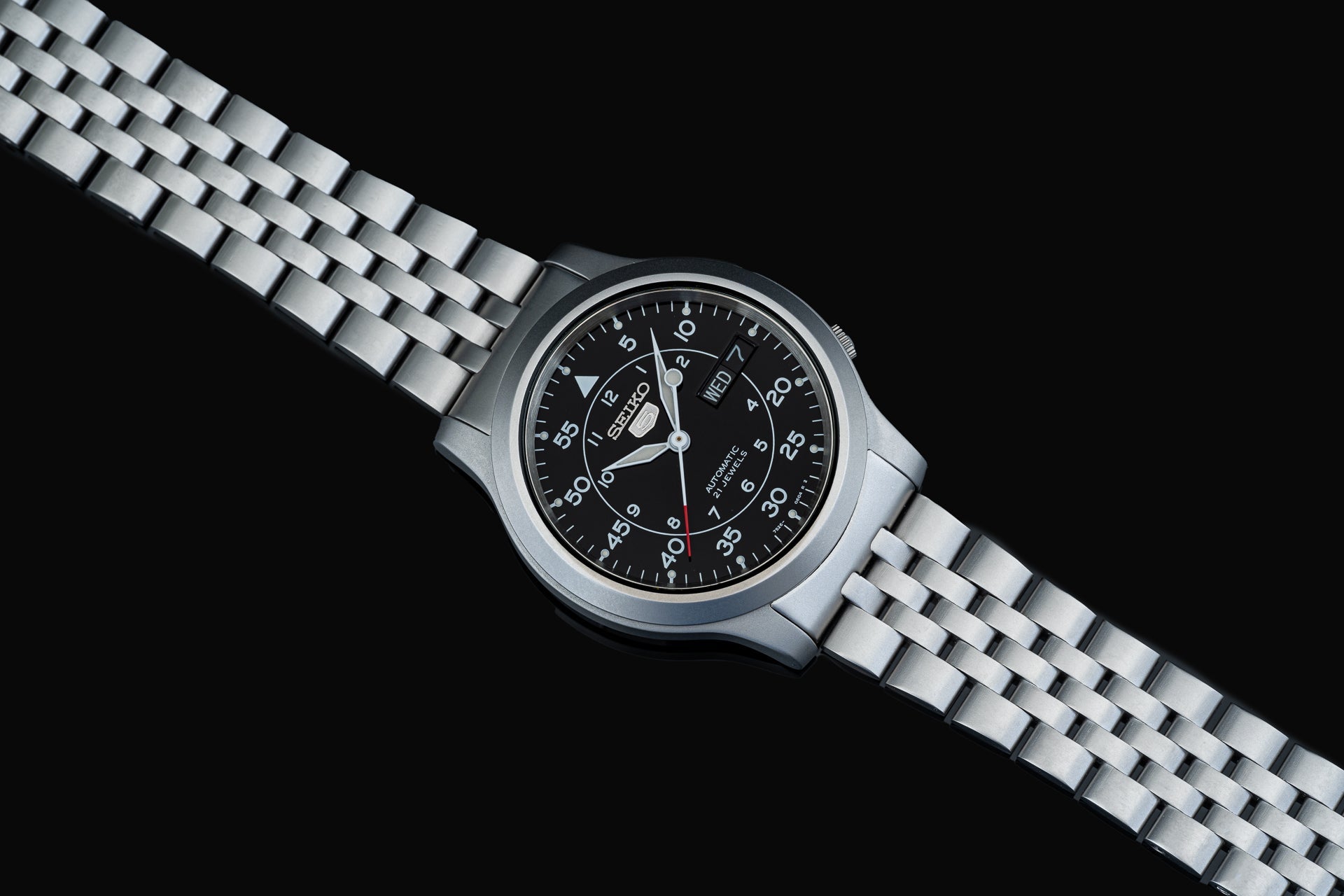 Seiko SNK80x automatic watch with black dial, day-date window, steel case and stainless steel bracelet on black background