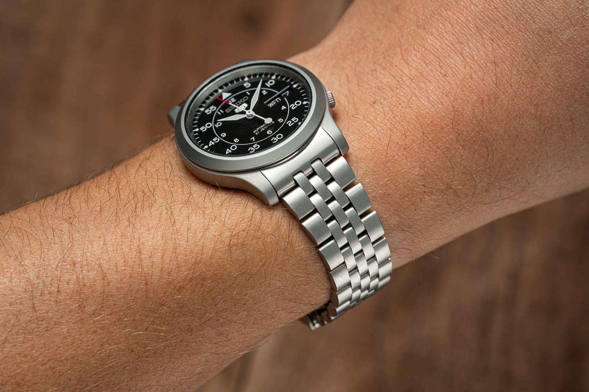Stainless steel automatic watch with black dial and Arabic numerals on wrist, featuring metal bracelet band