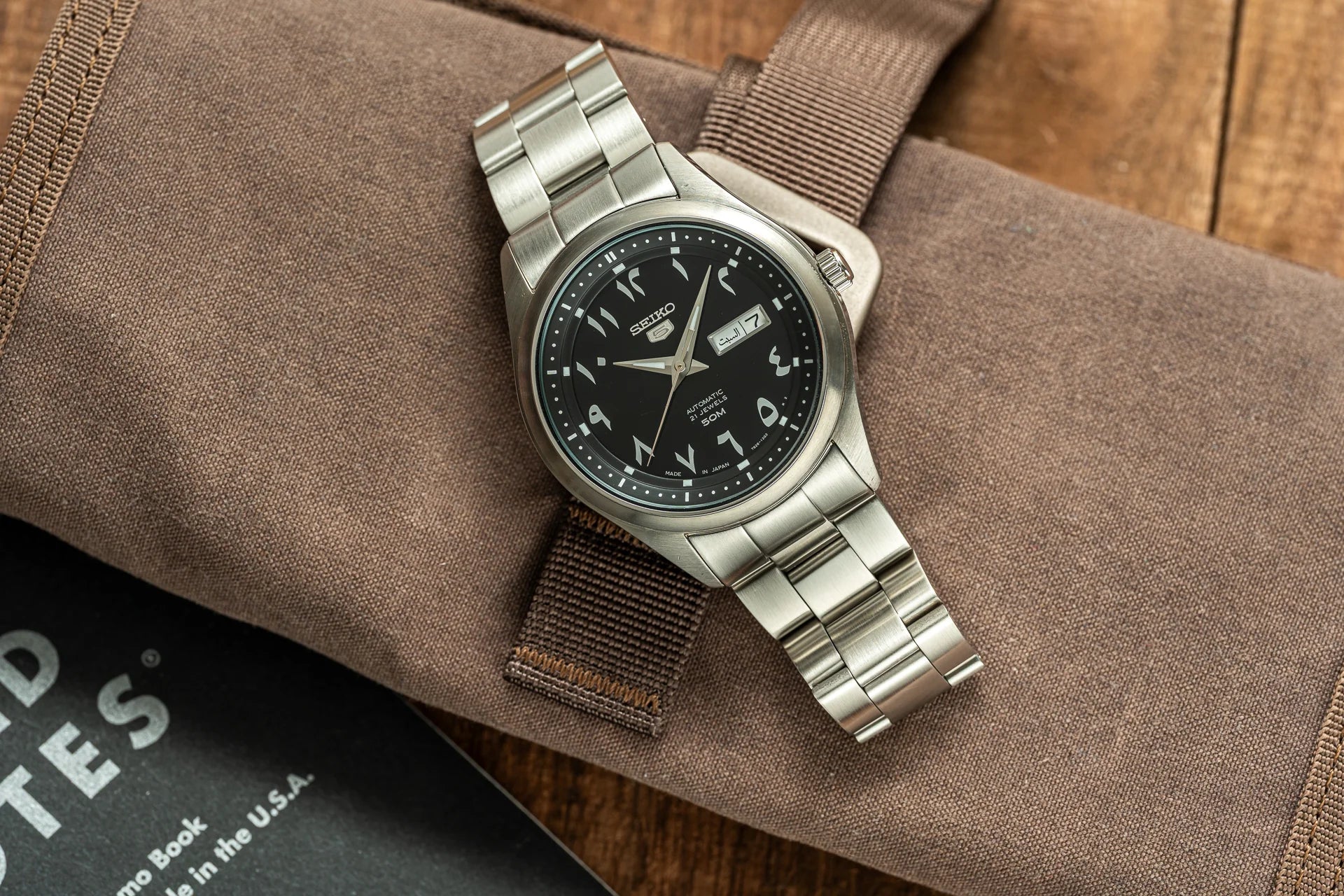 Seiko automatic watch with stainless steel bracelet, black dial, Arabic numerals, and day-date window on beige canvas strap