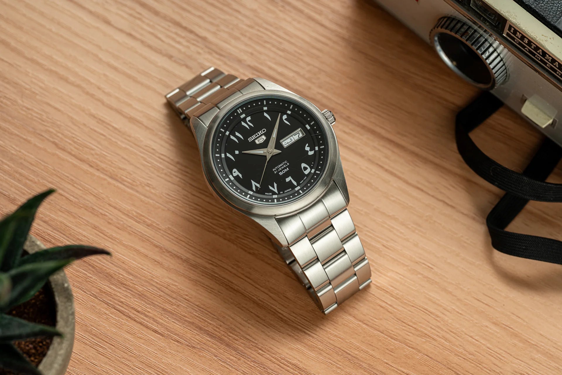 Seiko Senator automatic watch with Arabic numerals, black dial, stainless steel bracelet on wooden surface