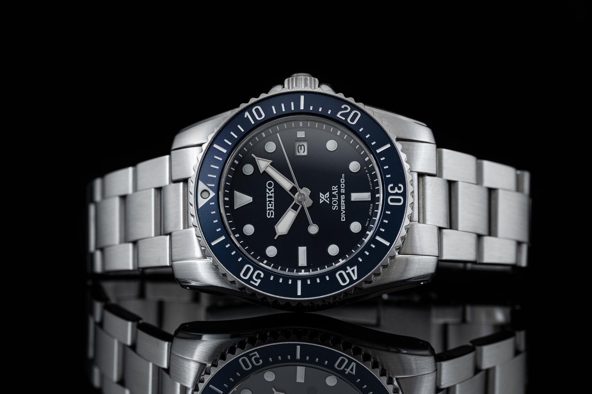 Seiko solar dive watch with stainless steel bracelet, black dial, rotating bezel, and silver hour markers on black background