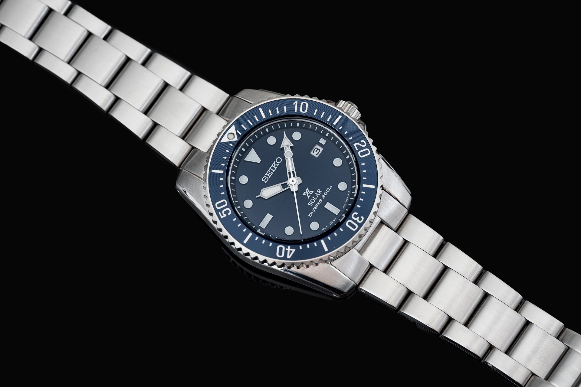 Seiko SNE57x solar dive watch with dark blue dial, stainless steel bracelet and rotating bezel on black background