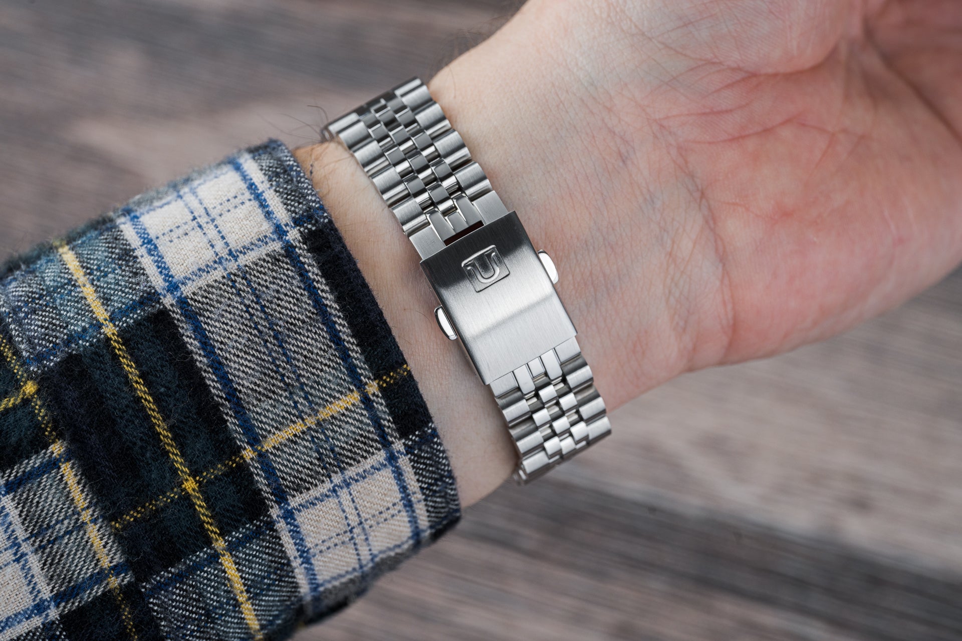 Stainless steel three-link bracelet watch on wrist with tartan sleeve, classic tool watch styling with integrated clasp