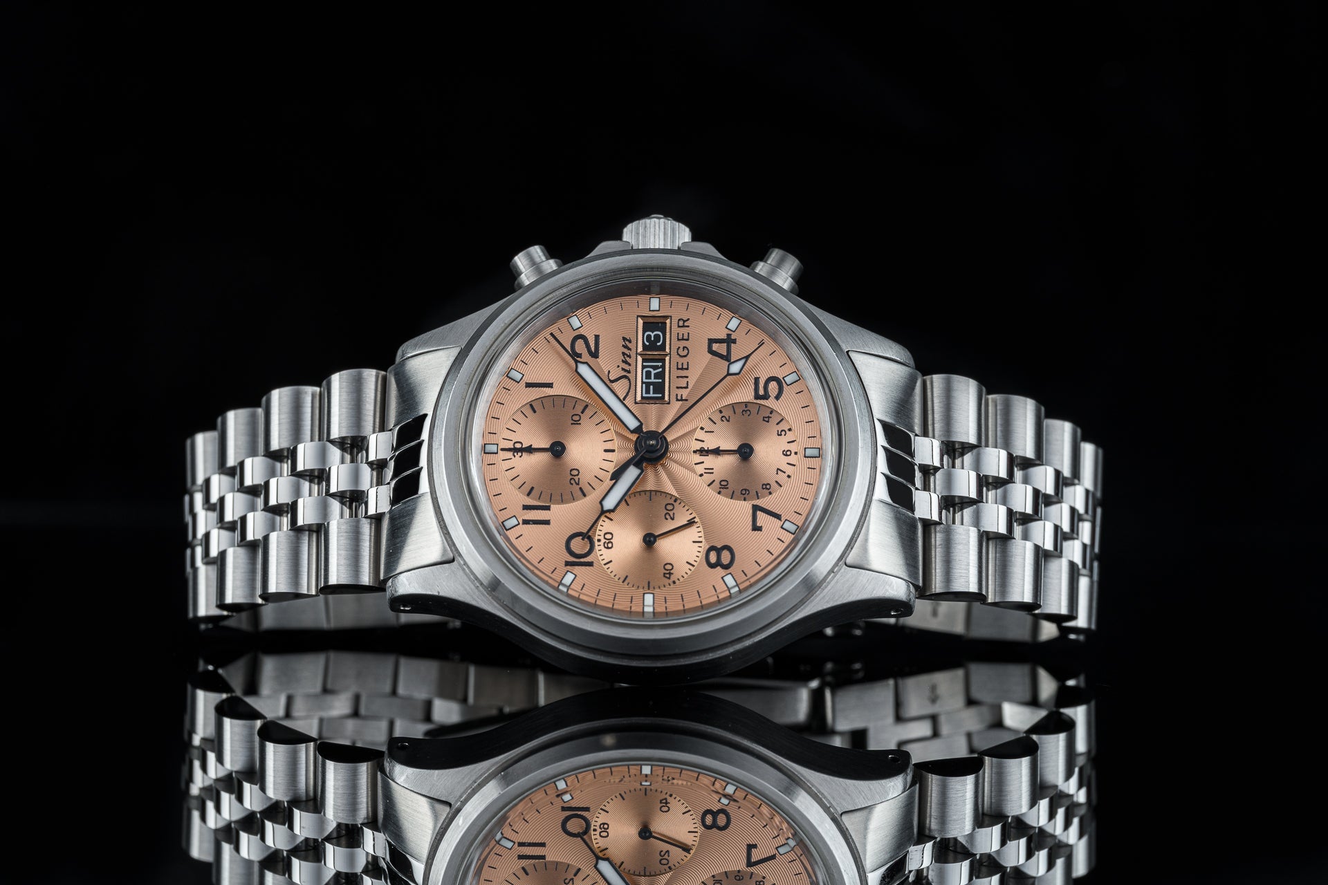 Stainless steel chronograph watch with salmon dial, day-date window, and linked bracelet on black background