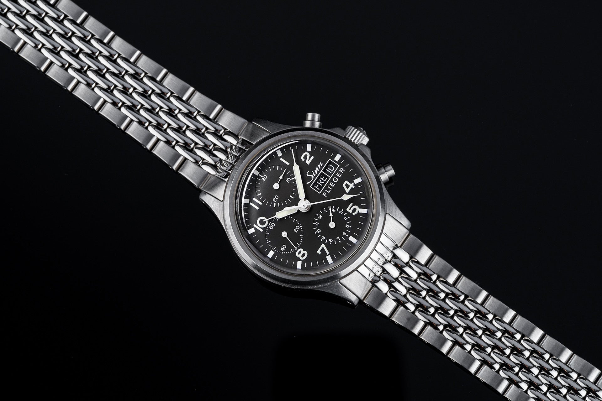 Sinn Flieger 356 chronograph watch with black dial and stainless steel Beads of Rice bracelet on black background