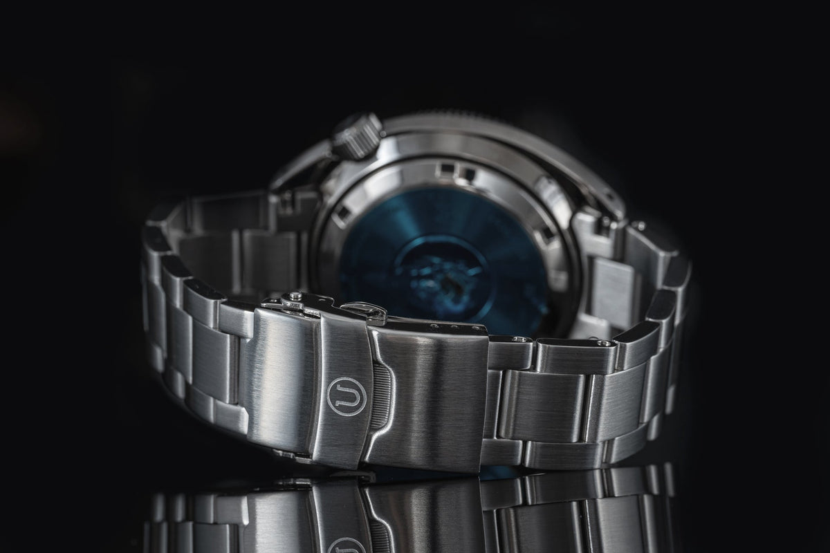 Stainless steel dive watch with blue dial and bracelet, rear view on black background showing clasp detail