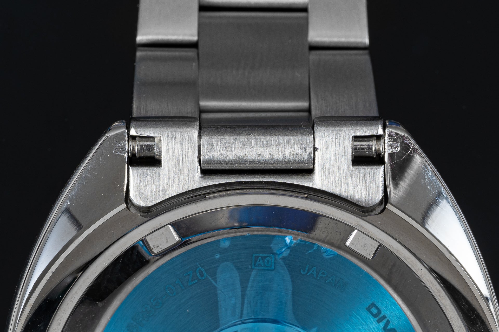 Stainless steel watch bracelet and lugs detail with brushed metal finish and blue dial visible