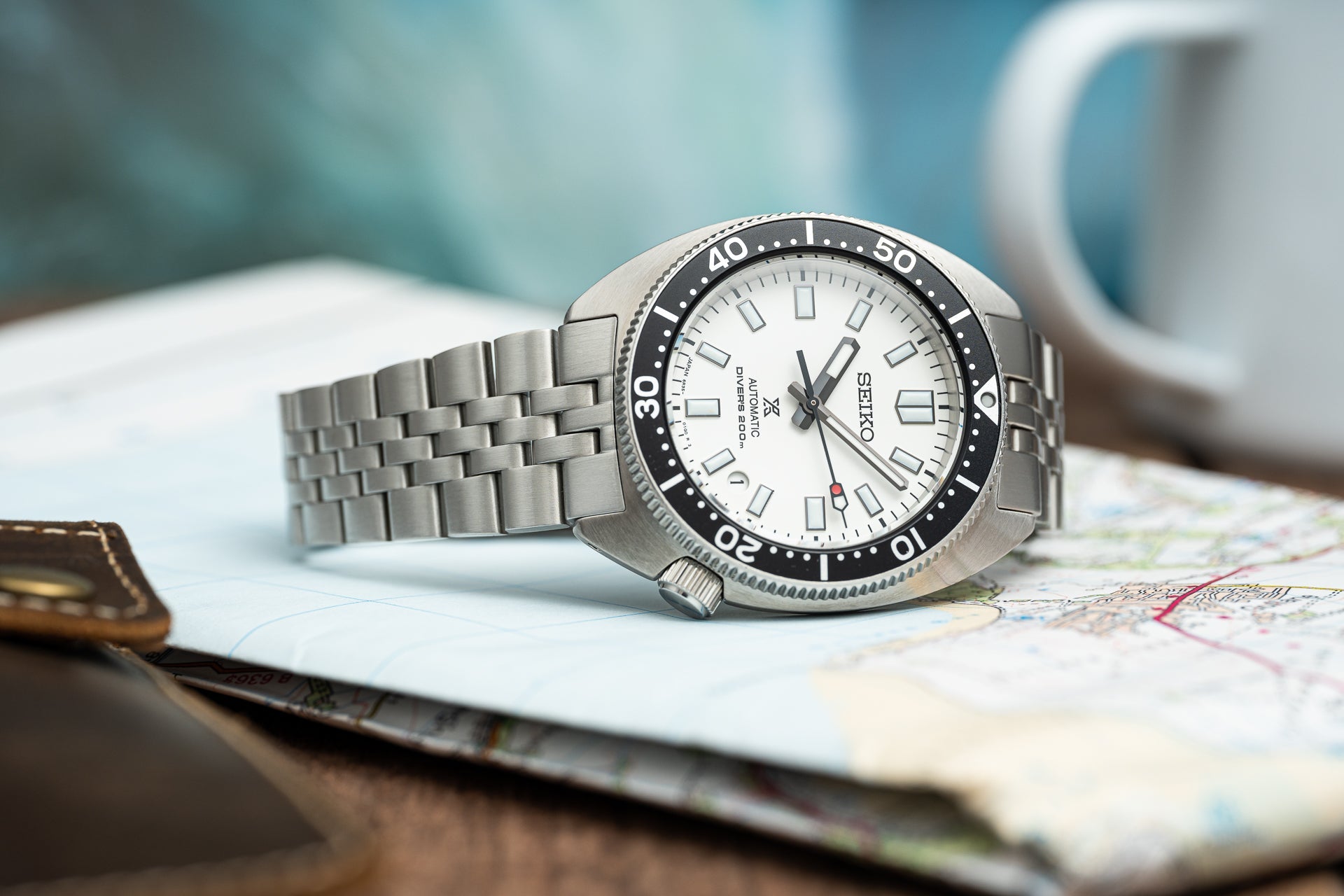 Seiko SPB31x Slim Turtle stainless steel dive watch with white dial, black bezel, and metal bracelet on map background