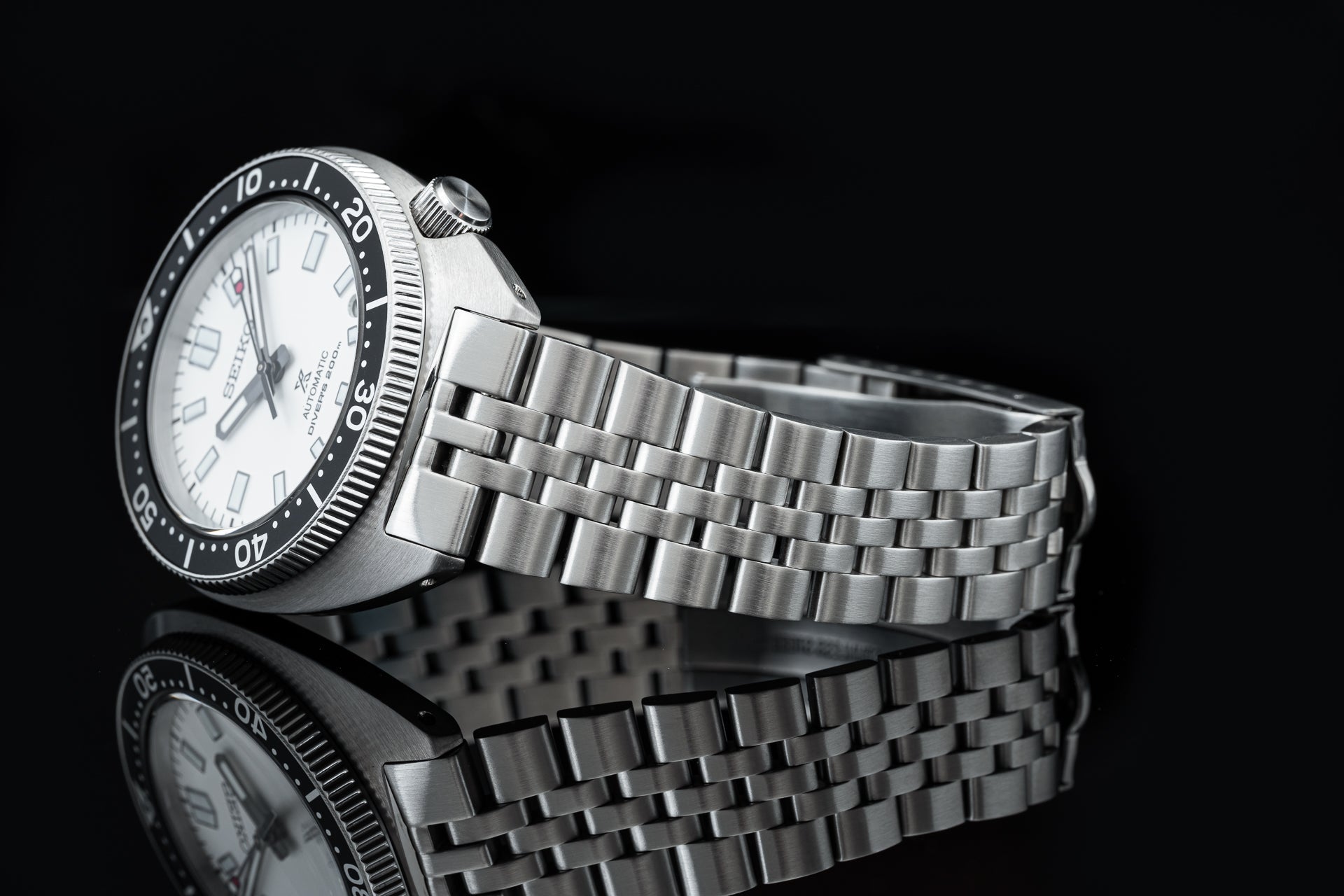 Seiko SPB31x Slim Turtle dive watch with white dial, black bezel, and stainless steel jubilee bracelet on black background