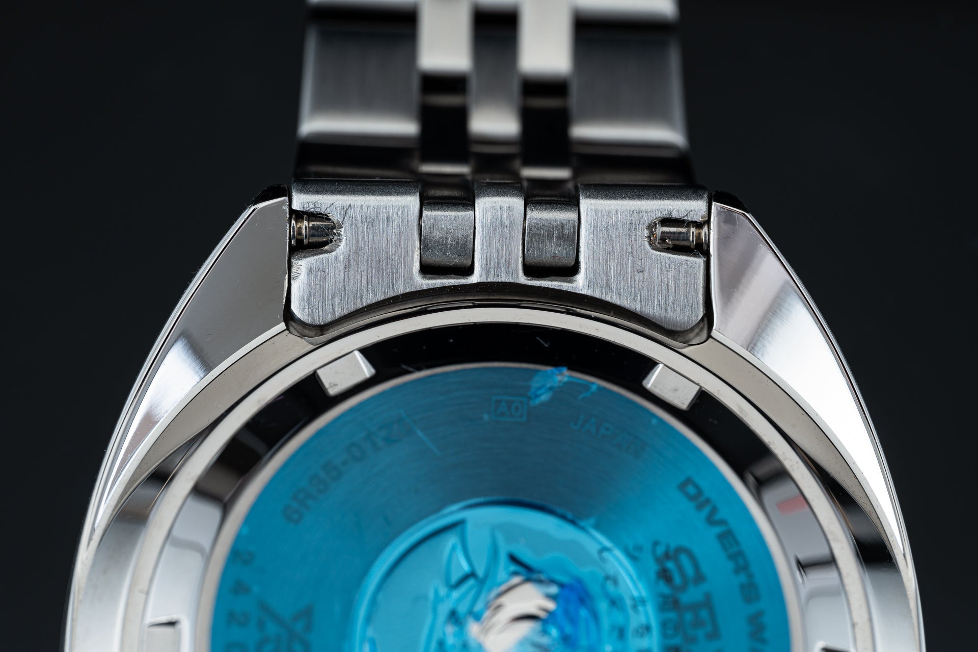 Stainless steel watch bracelet and clasp detail with blue dial showing, polished metal links and secure fastening mechanism