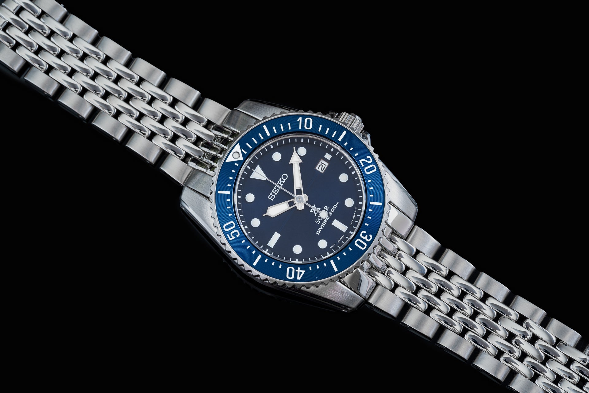 Seiko Solar dive watch with blue bezel, dark dial, and stainless steel bracelet on black background