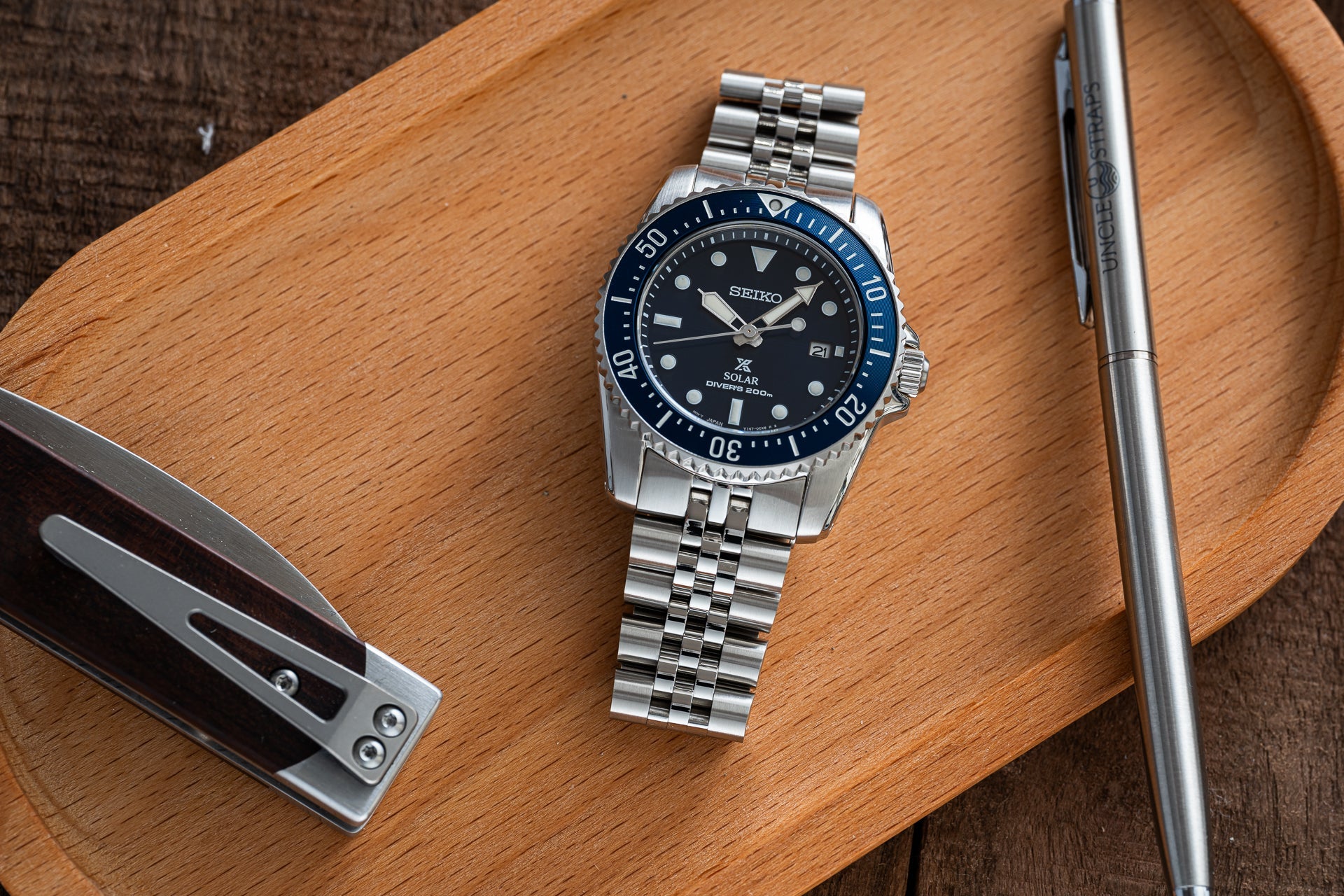 Seiko Solar dive watch with stainless steel bracelet and black dial on wooden desk with pen