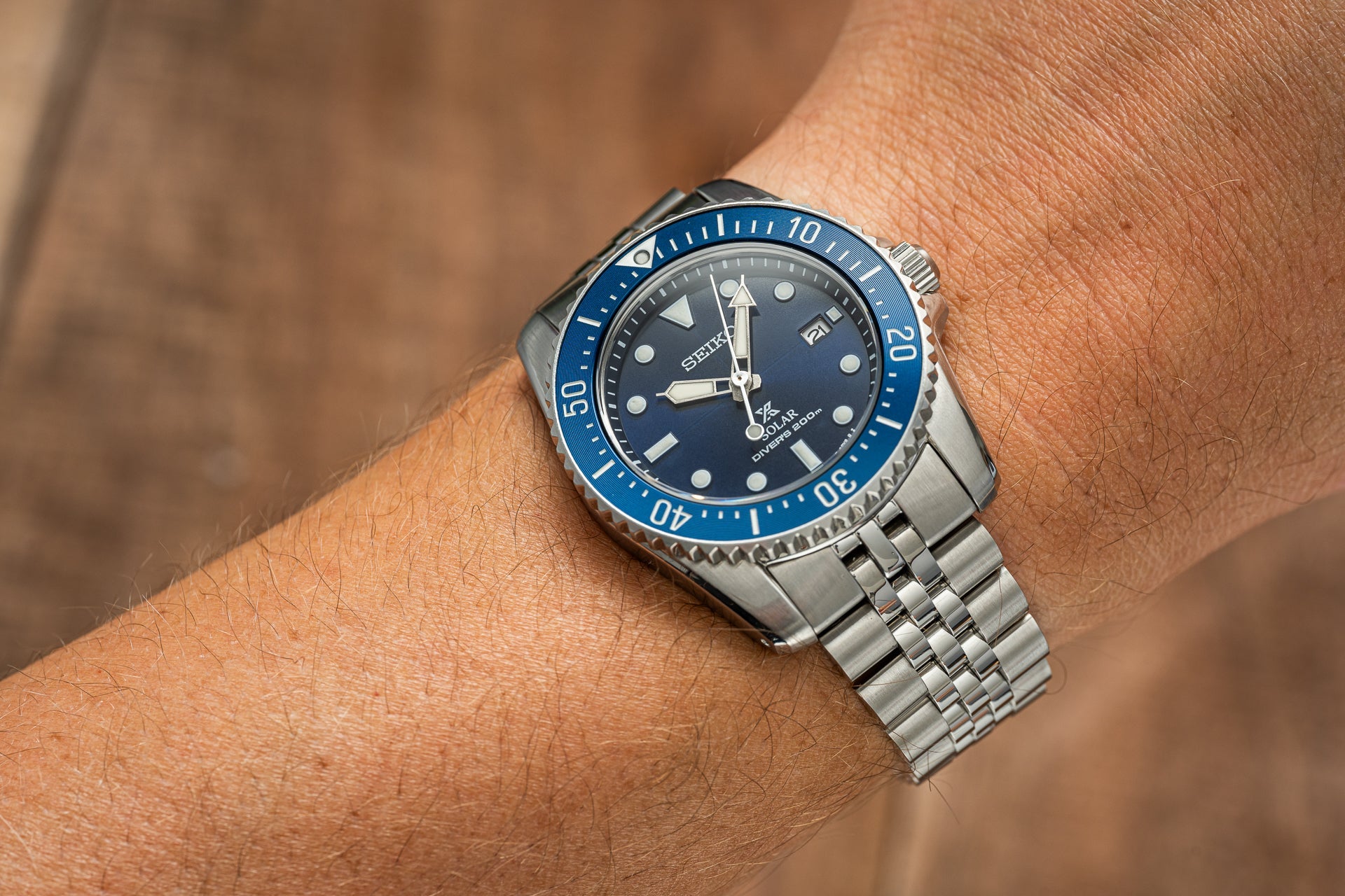 Silver stainless steel dive watch with blue bezel and dark dial on jubilee bracelet worn on wrist
