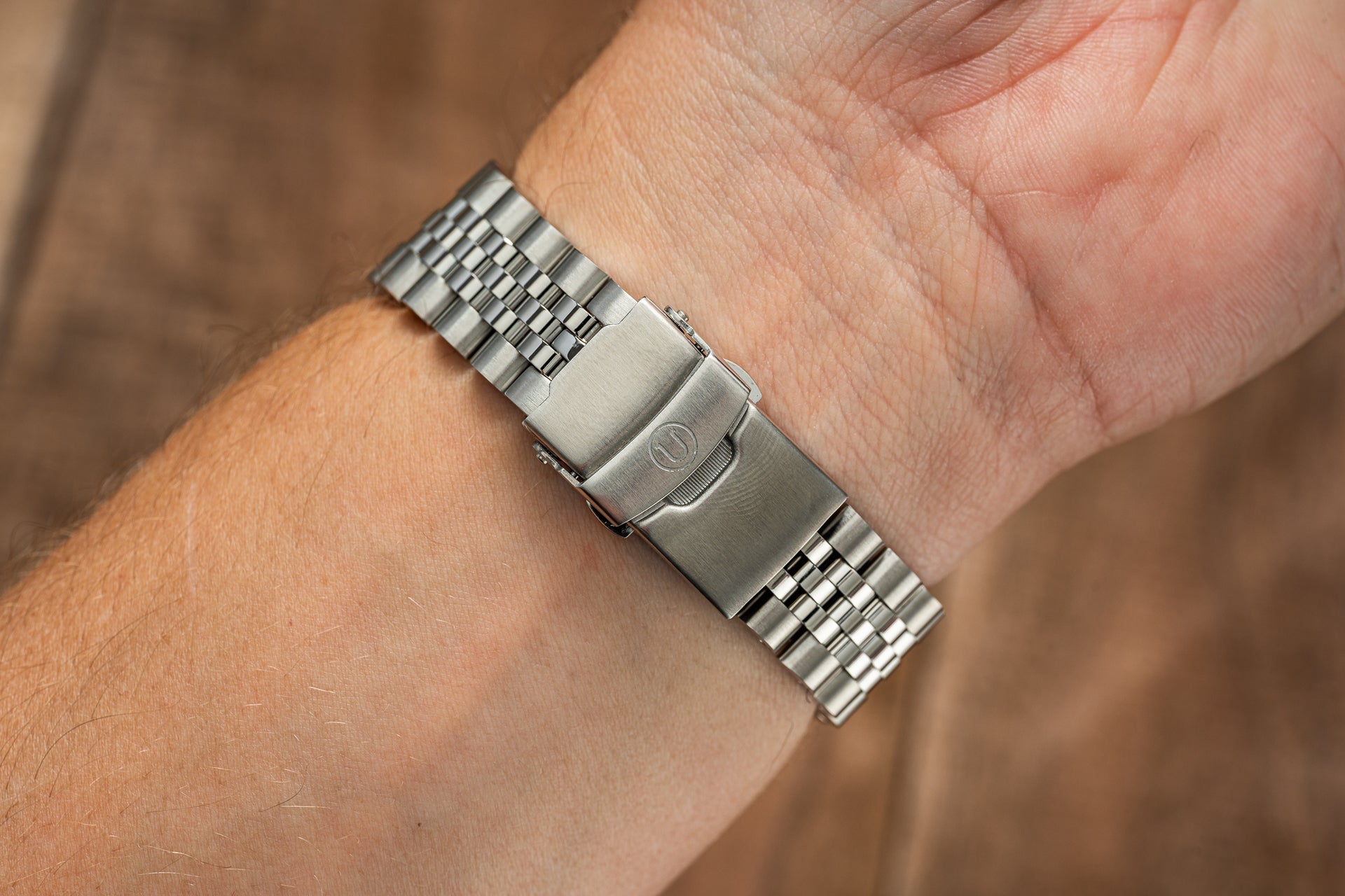 Brushed stainless steel solar watch bracelet with deployant clasp worn on wrist, close-up detail shot