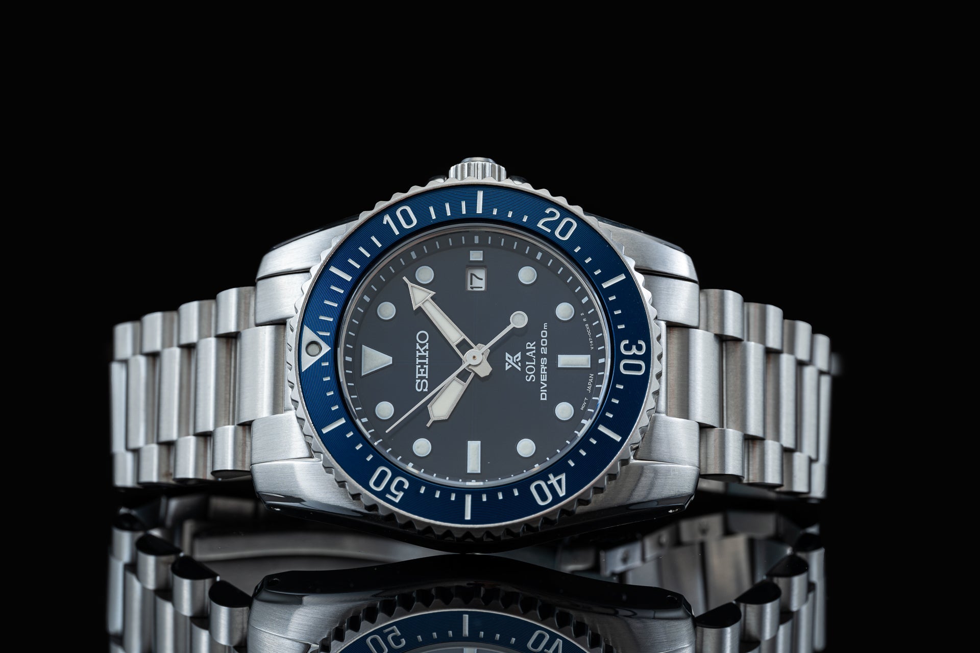 Seiko Solar dive watch with blue bezel, stainless steel bracelet, dark dial and date window against black background