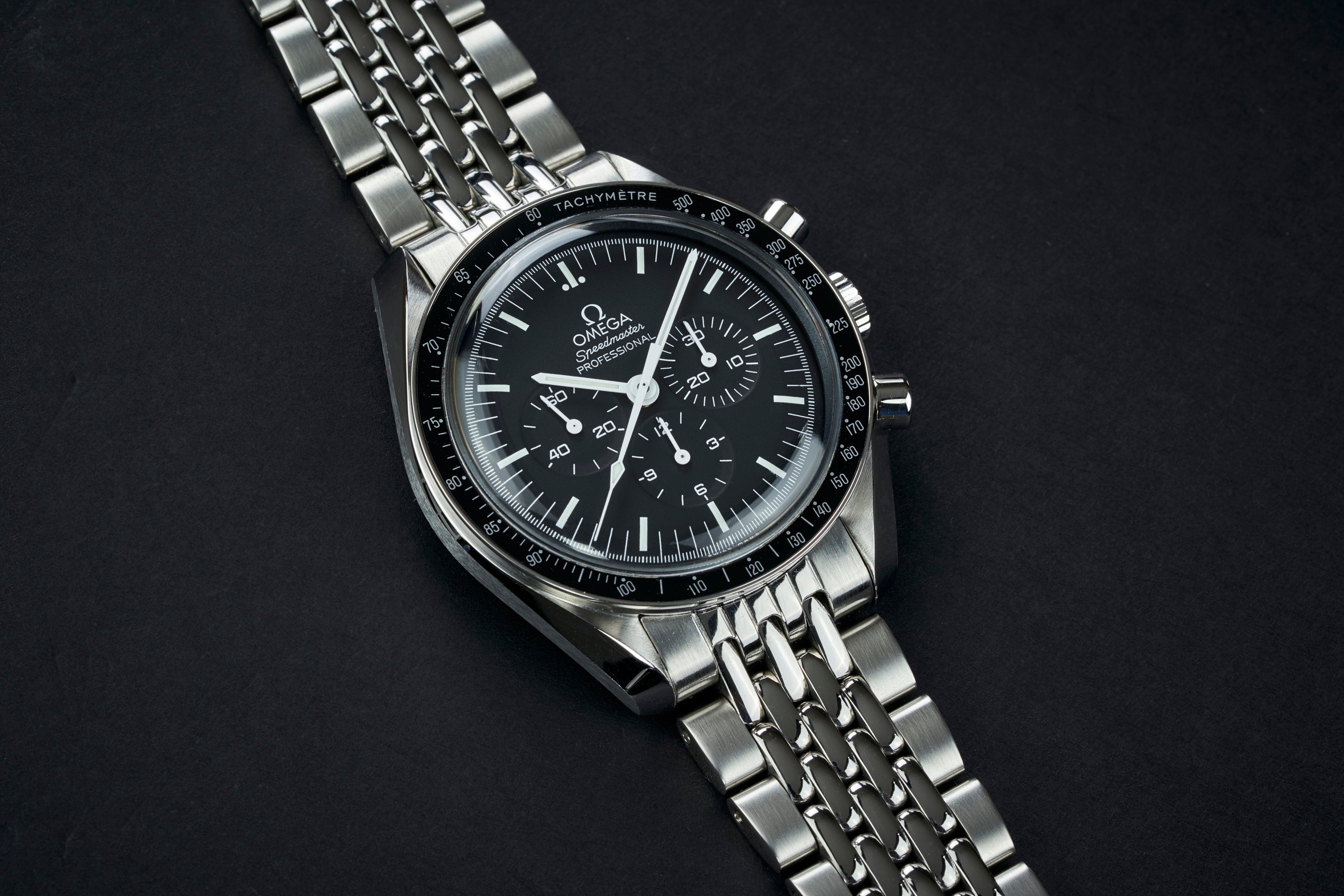 Omega Speedmaster Professional chronograph watch with black dial, tachymetre bezel, and steel Beads of Rice bracelet