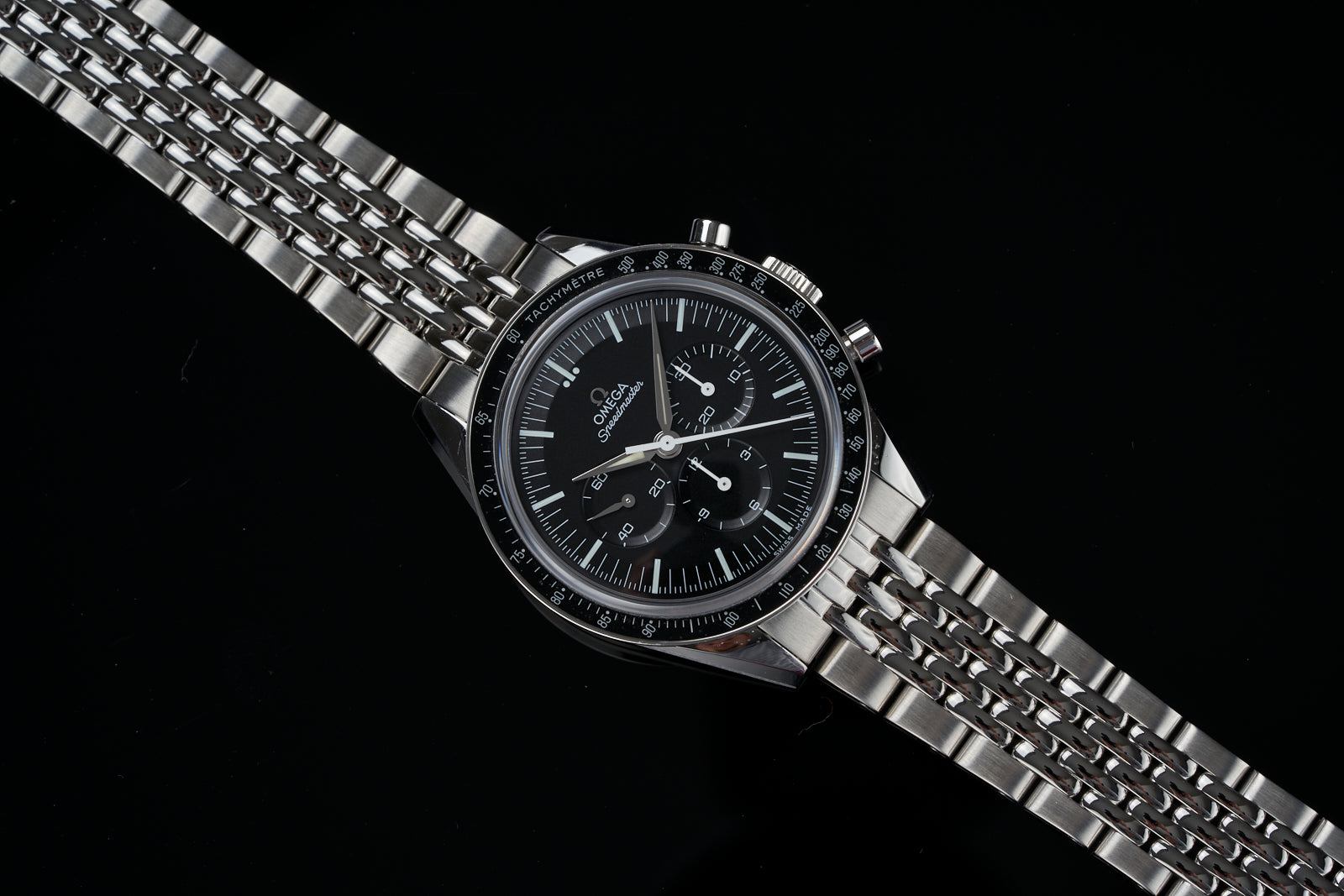Omega Speedmaster chronograph watch with black dial, tachymeter bezel, and stainless steel Beads of Rice bracelet on black background