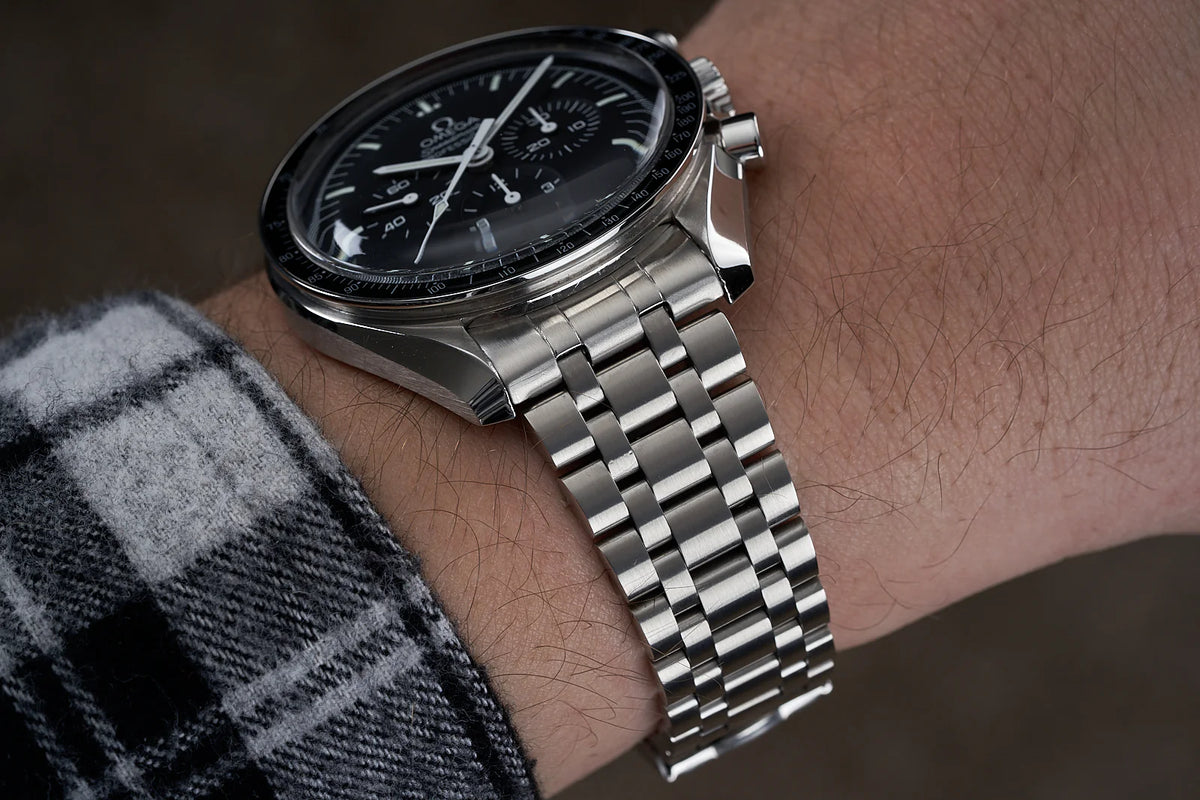 Omega Speedmaster Professional chronograph watch with black dial and stainless steel bracelet worn on wrist with grey sweater
