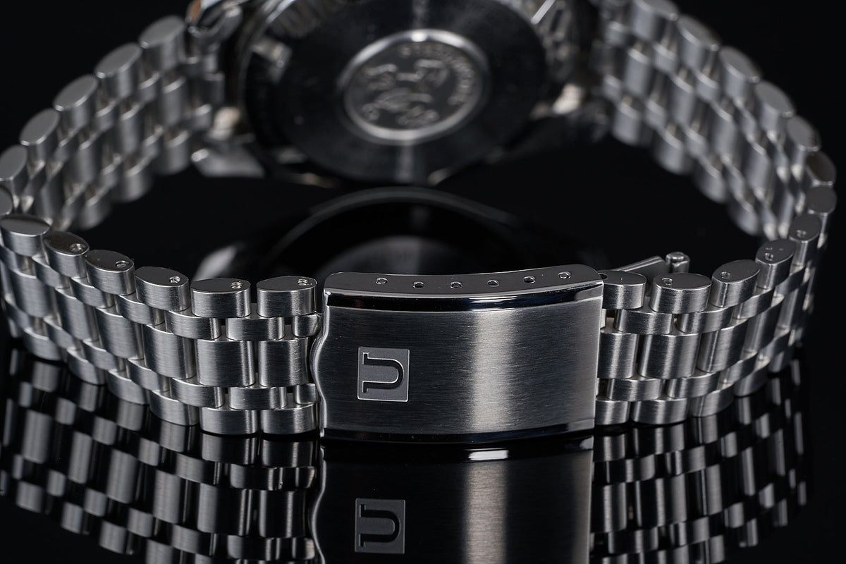 Stainless steel watch bracelet with polished link segments and branded clasp, displayed on black background