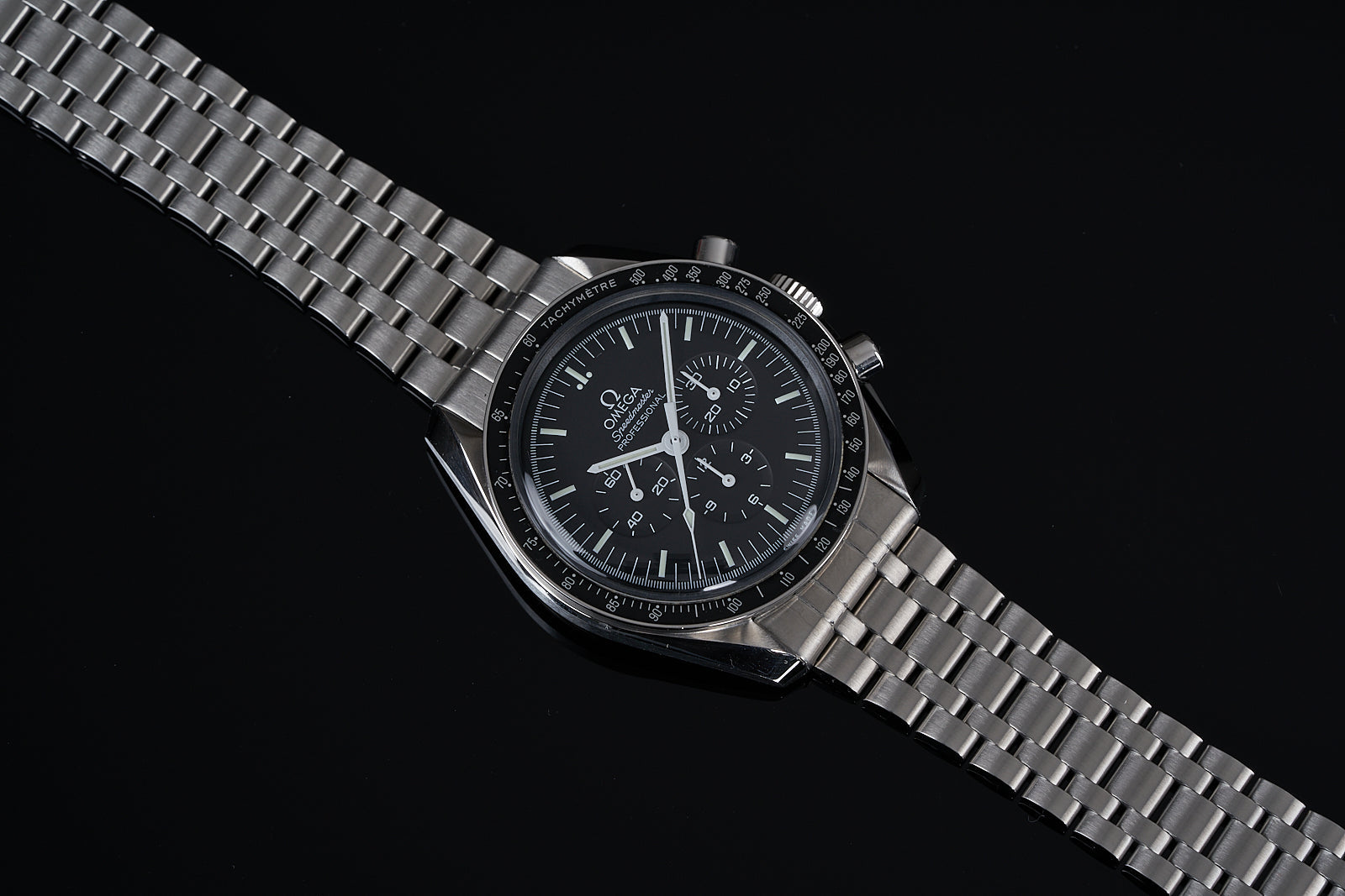 Stainless steel chronograph watch with black dial, tachymetre bezel, and metal bracelet on black background