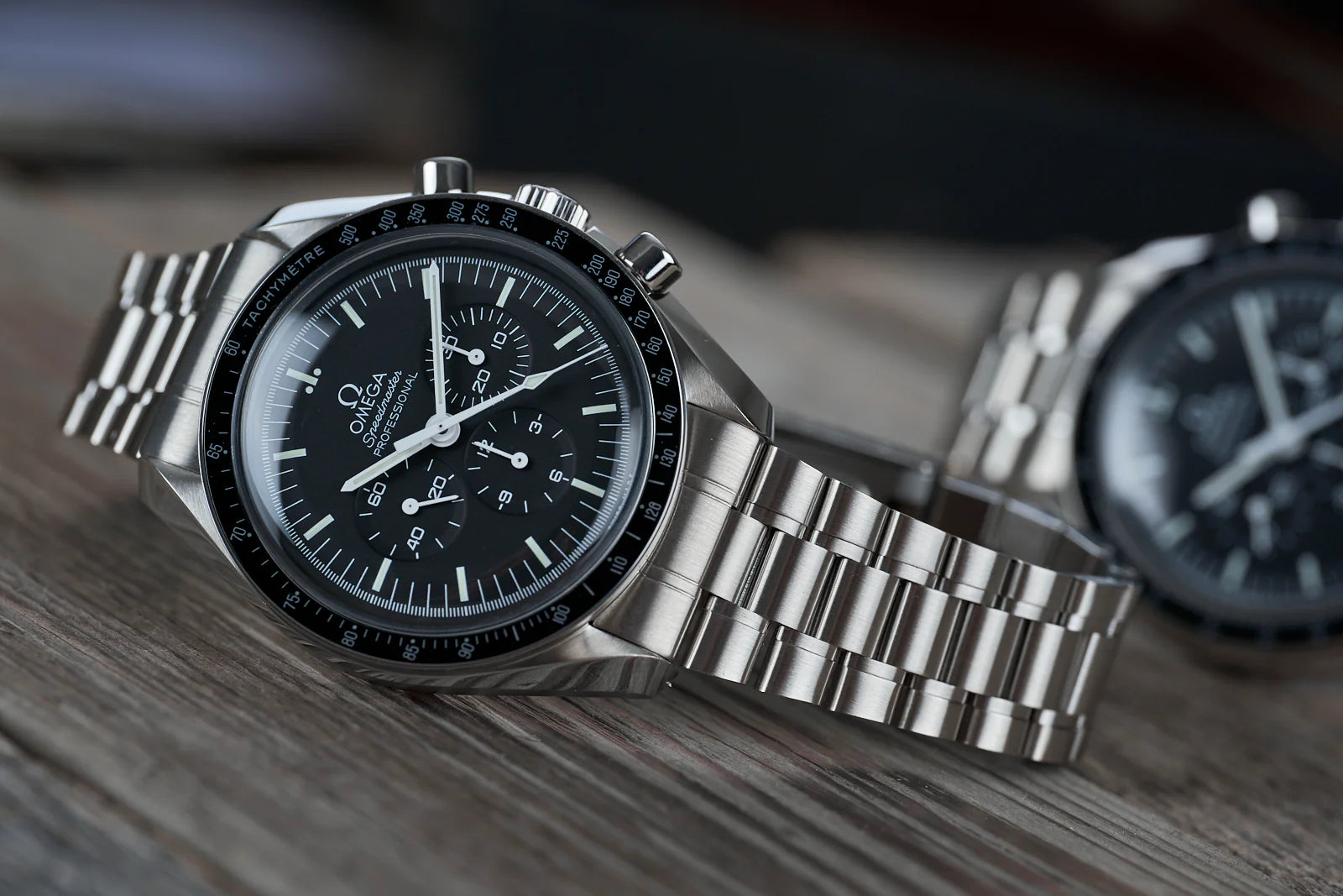 Omega Speedmaster Professional chronograph watch with stainless steel bracelet and black dial on wooden surface