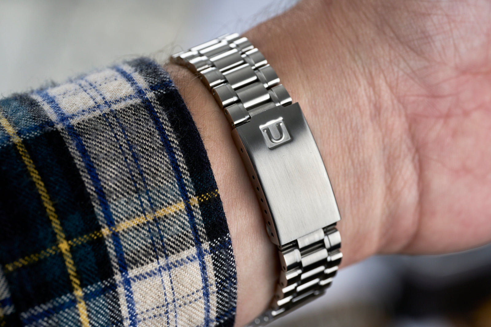 Stainless steel link bracelet with polished and brushed finish worn on wrist with plaid sleeve