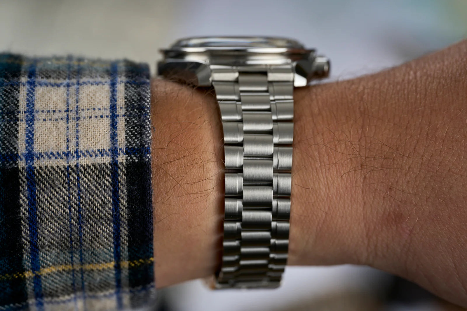 Silver stainless steel bracelet watch with metal links worn on wrist over blue plaid shirt sleeve