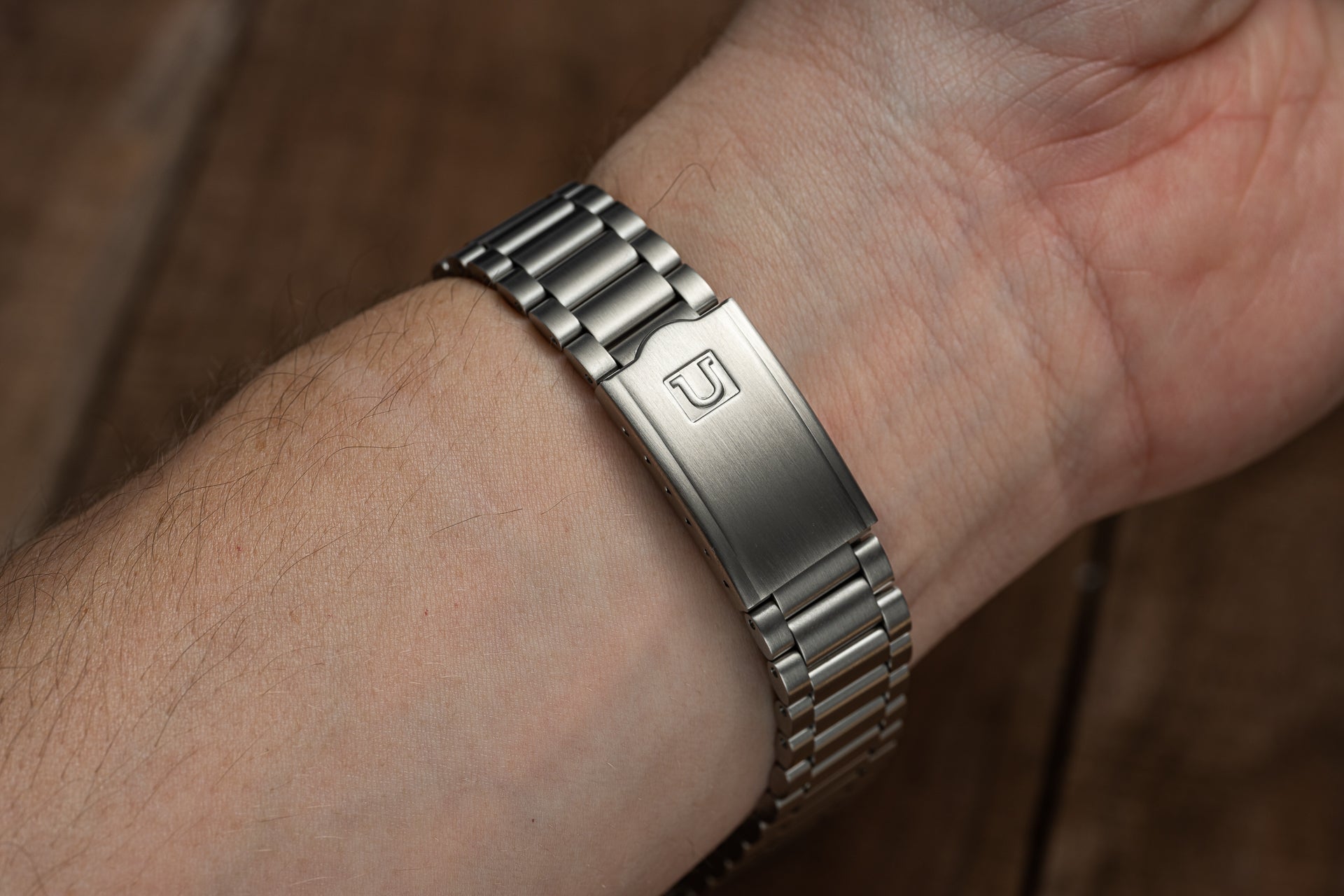 Stainless steel watch bracelet with polished and brushed links worn on wrist, featuring engraved logo clasp
