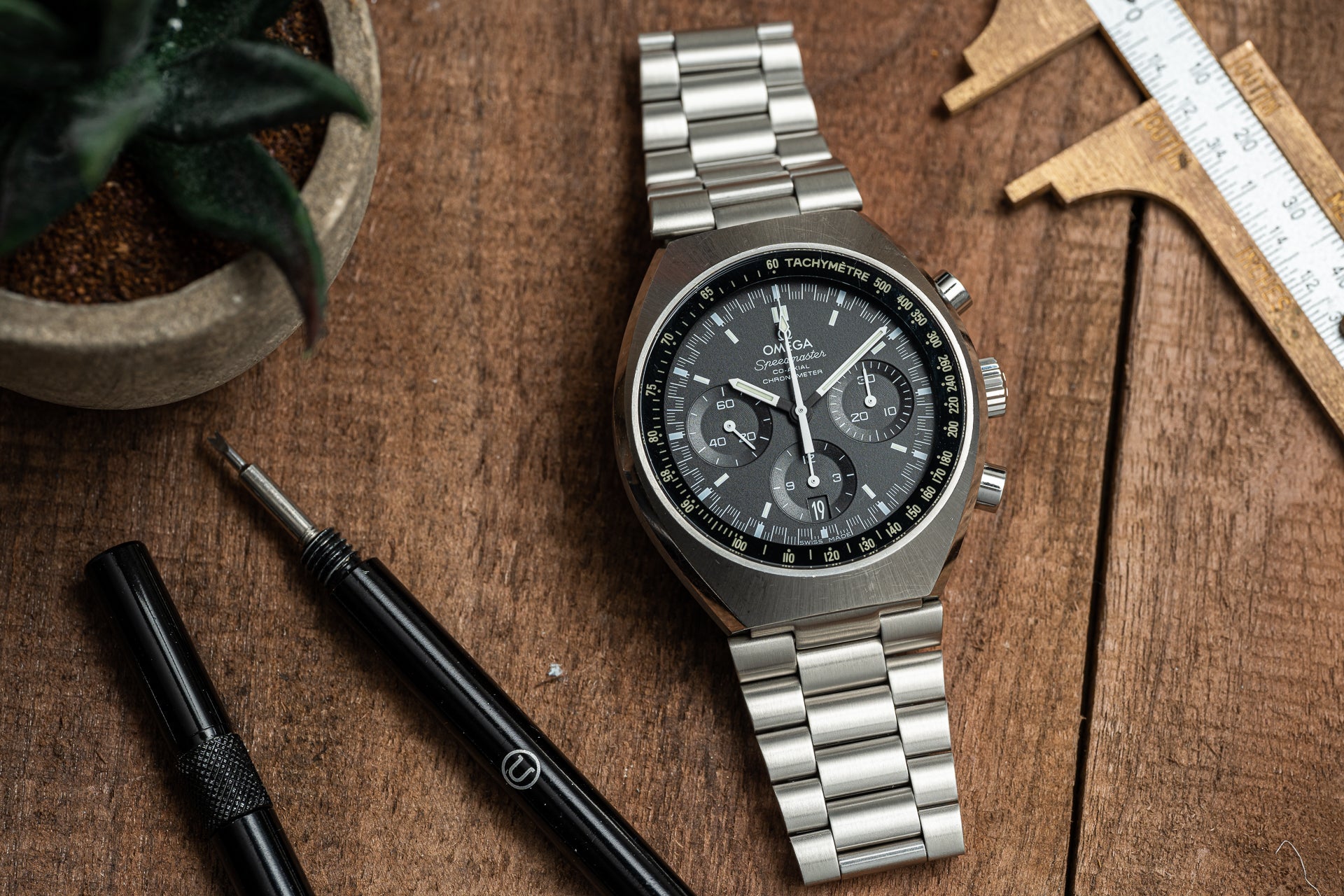 Omega Speedmaster Mark II chronograph watch with stainless steel bracelet and black dial on wooden workbench with tools