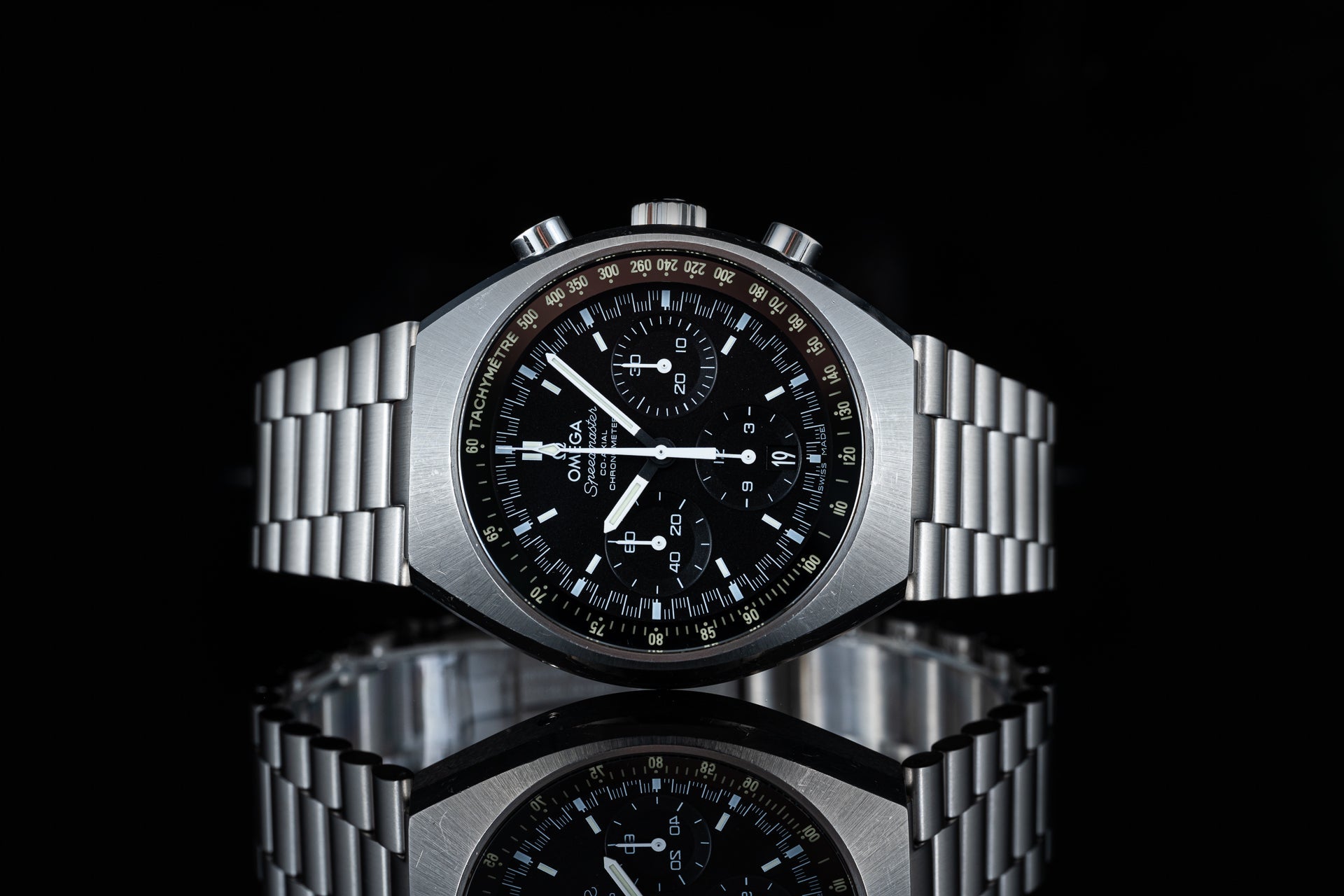 Omega Speedmaster Mark II chronograph watch with stainless steel bracelet and black dial on reflective surface