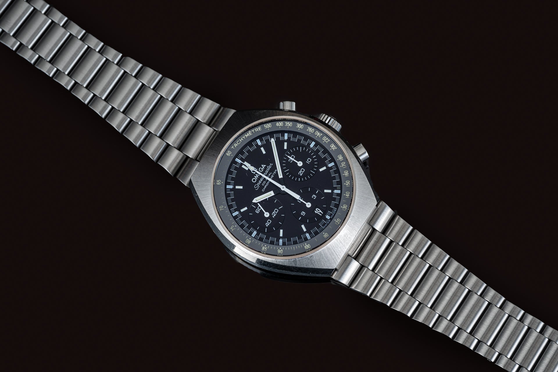 Omega Speedmaster Mark II chronograph watch with black dial, stainless steel case and metal bracelet on dark background