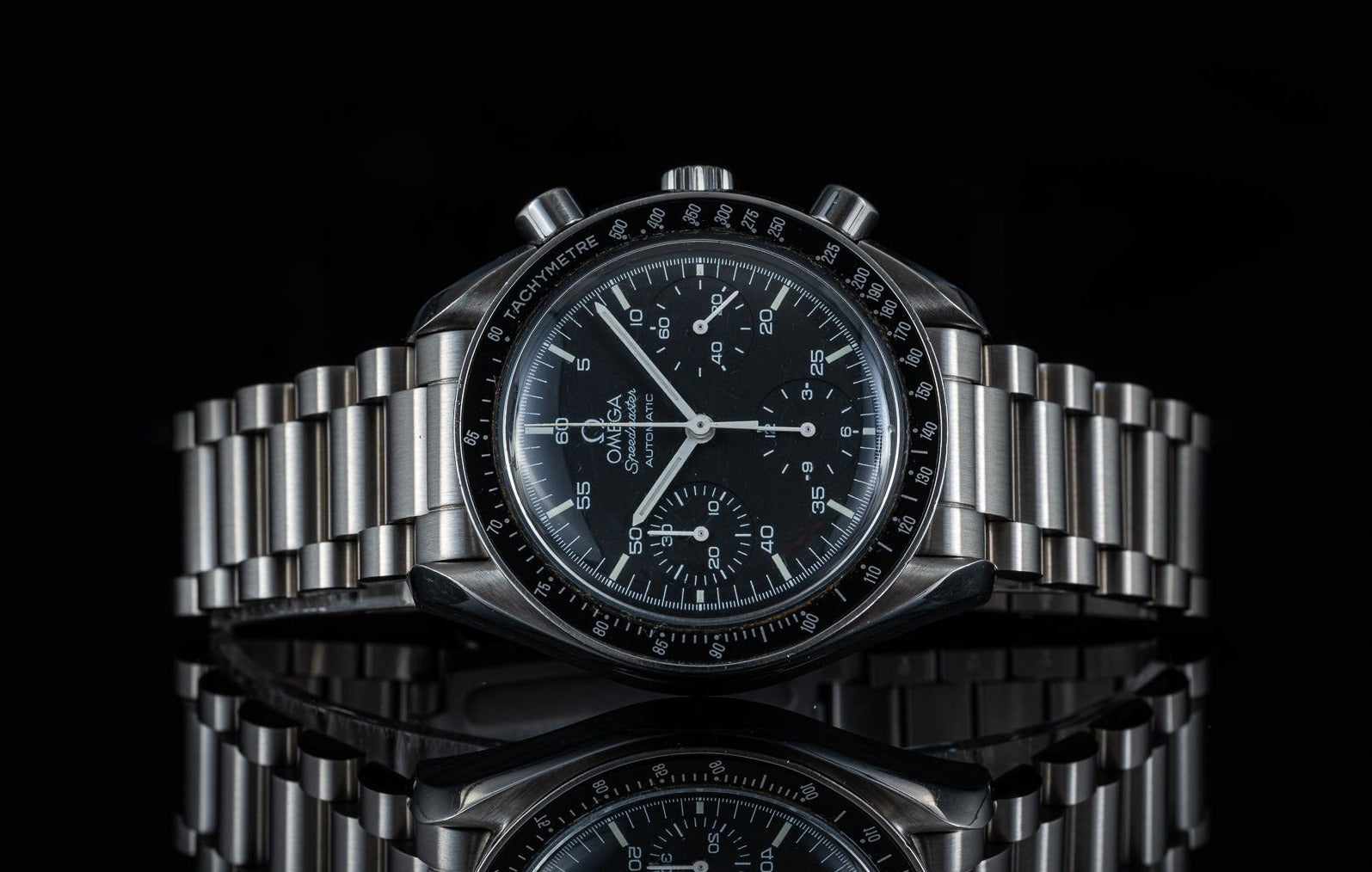 Omega Speedmaster Reduced automatic chronograph watch with stainless steel bracelet and black dial on black background