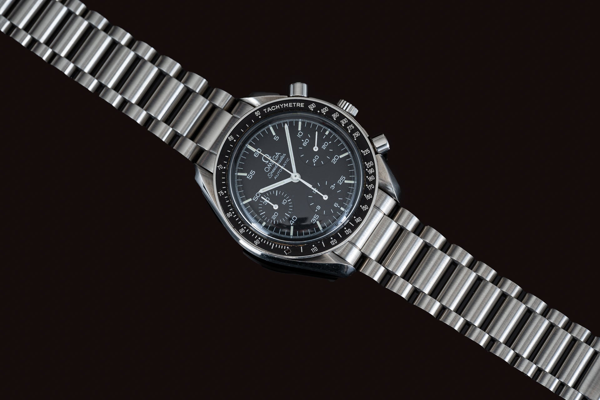 Omega Speedmaster Reduced chronograph watch with black dial, tachymetre bezel, and stainless steel bracelet on black background