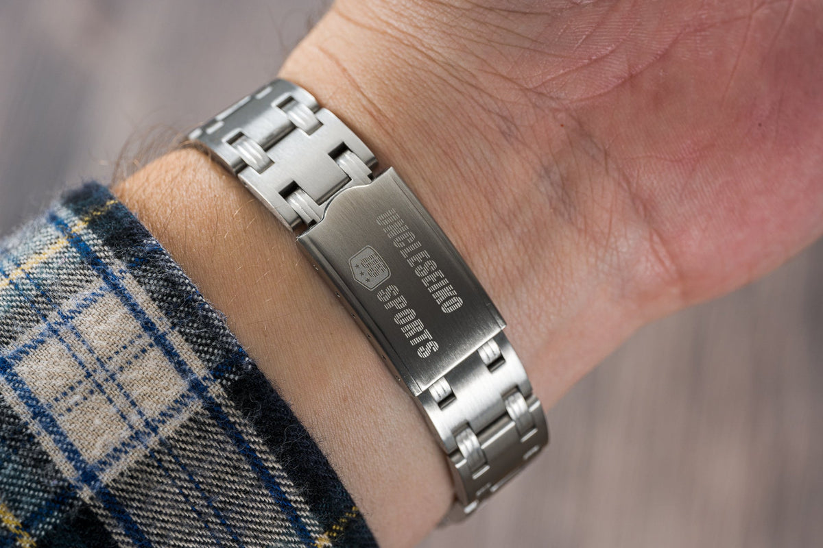 Silver stainless steel digital watch bracelet with rectangular face worn on wrist over plaid fabric sleeve