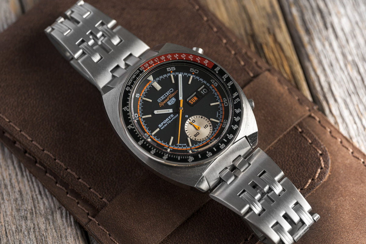 Seiko Speedtimer chronograph watch with black dial, orange accents, steel bracelet and tachymeter bezel on leather background