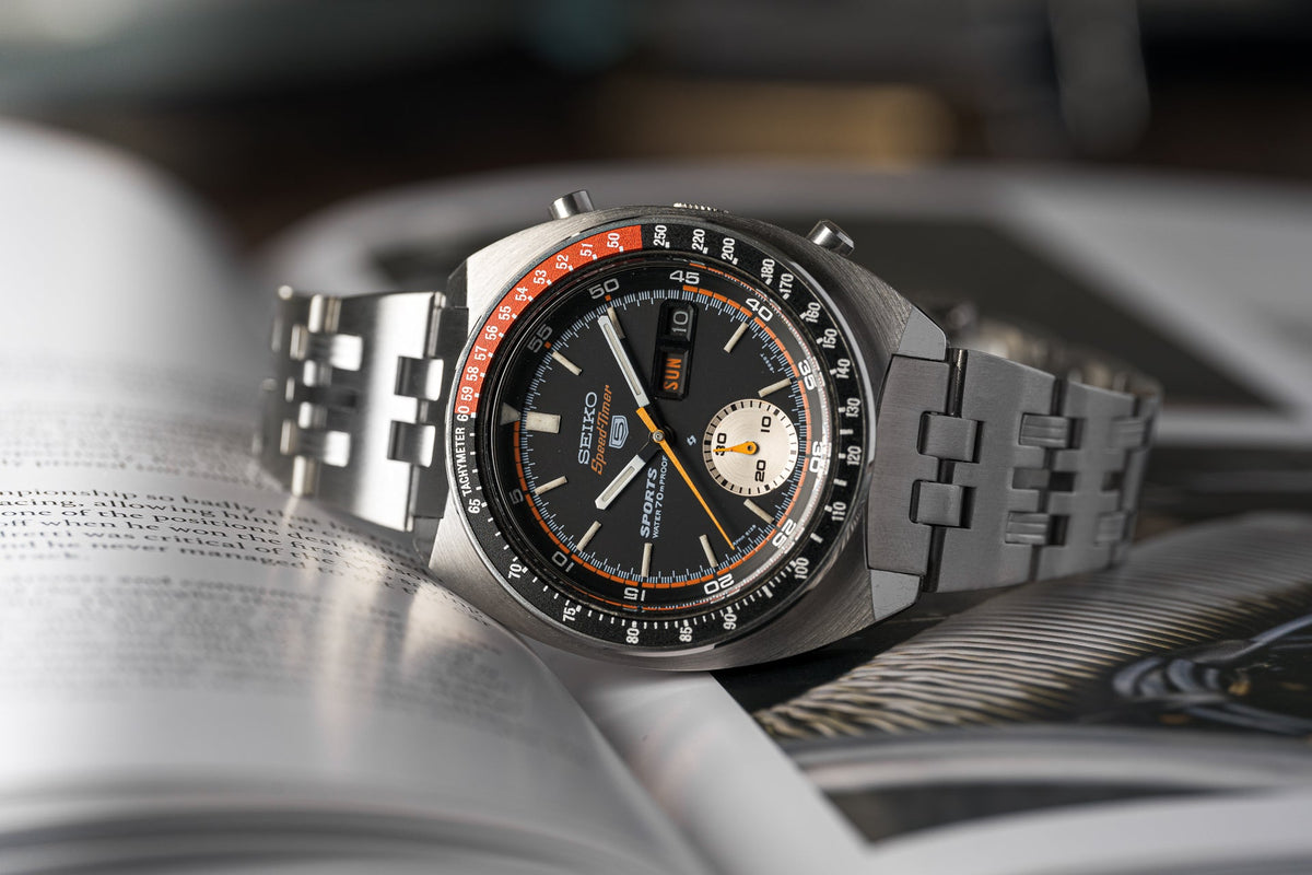 Seiko Speedtimer vintage chronograph watch with black dial, orange accents, and stainless steel bracelet on open book