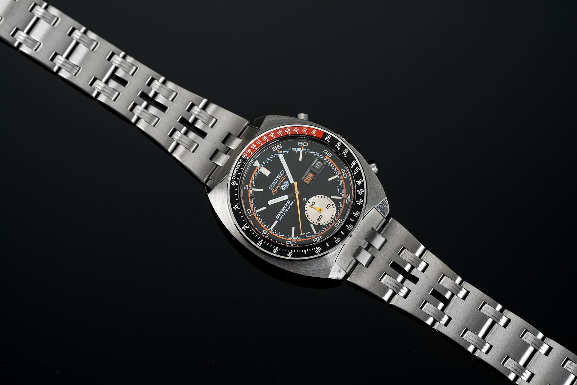 Vintage Seiko Speedtimer chronograph watch with black dial, orange accents, steel bracelet and rotating bezel on black background