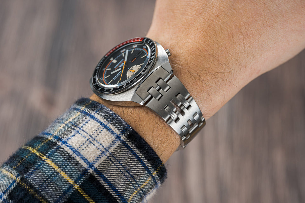 Seiko Speedtimer vintage watch with black dial and orange accents on stainless steel bracelet, worn on wrist with plaid shirt