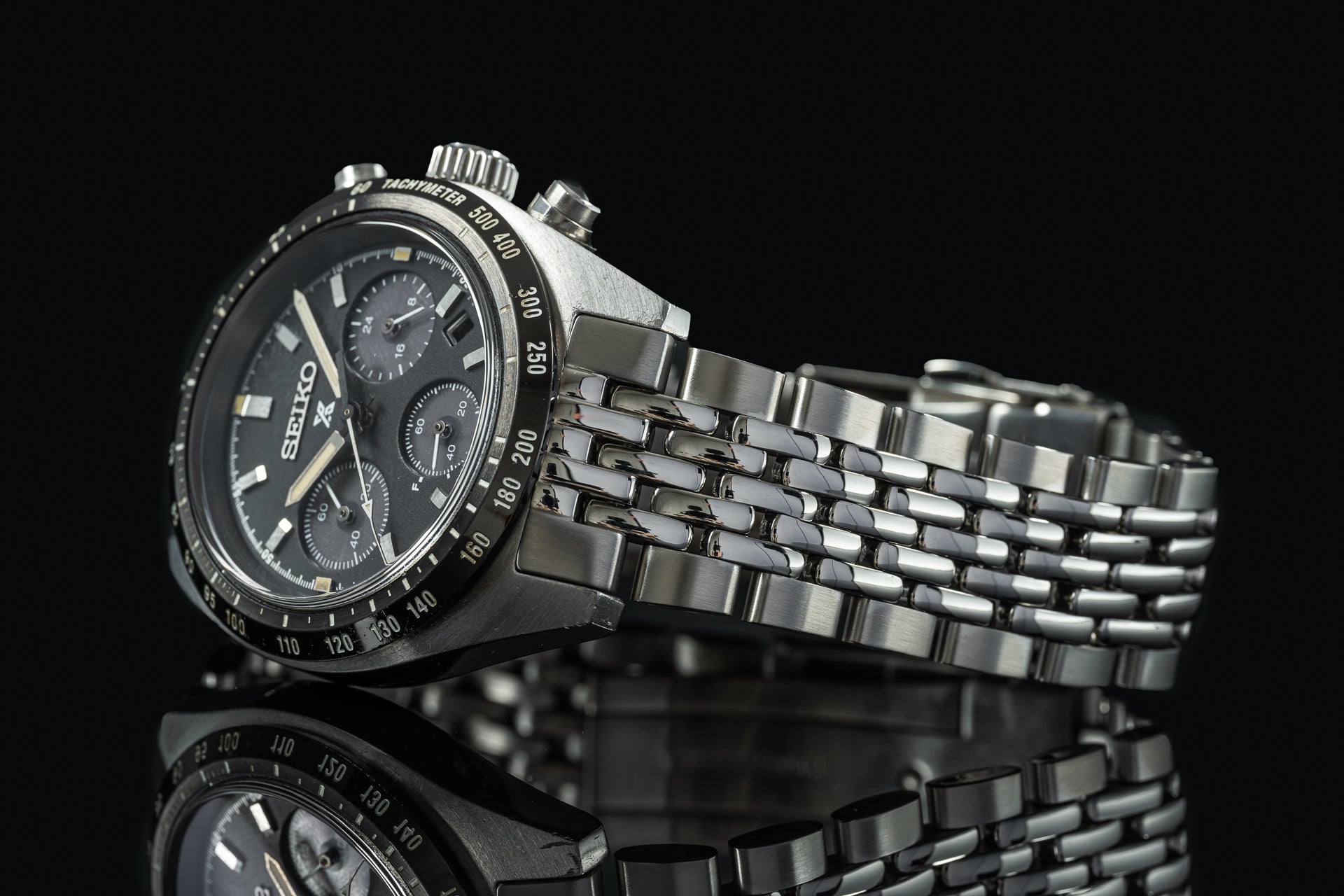 Seiko Speedtimer chronograph watch with black dial, tachymeter bezel, and stainless steel jubilee bracelet on black background