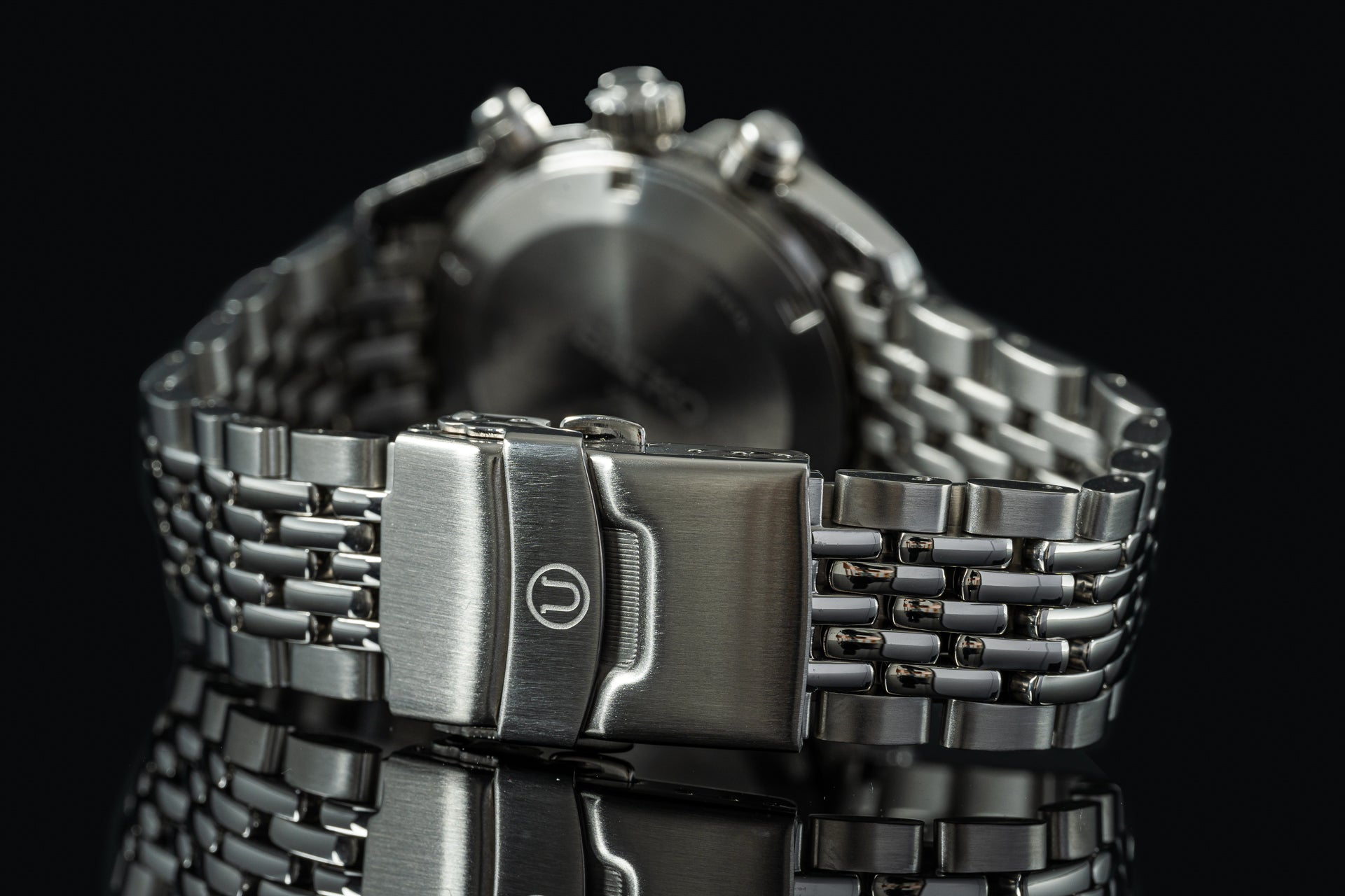Stainless steel chronograph watch with beads of rice bracelet and push-button clasp on black background