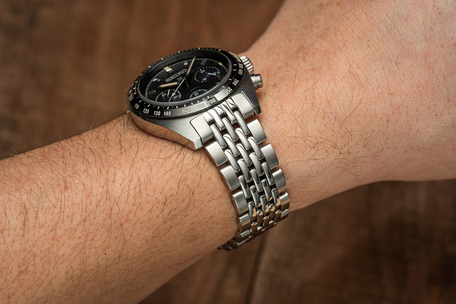 Men's chronograph watch with black dial and tachymeter bezel on stainless steel bracelet worn on wrist
