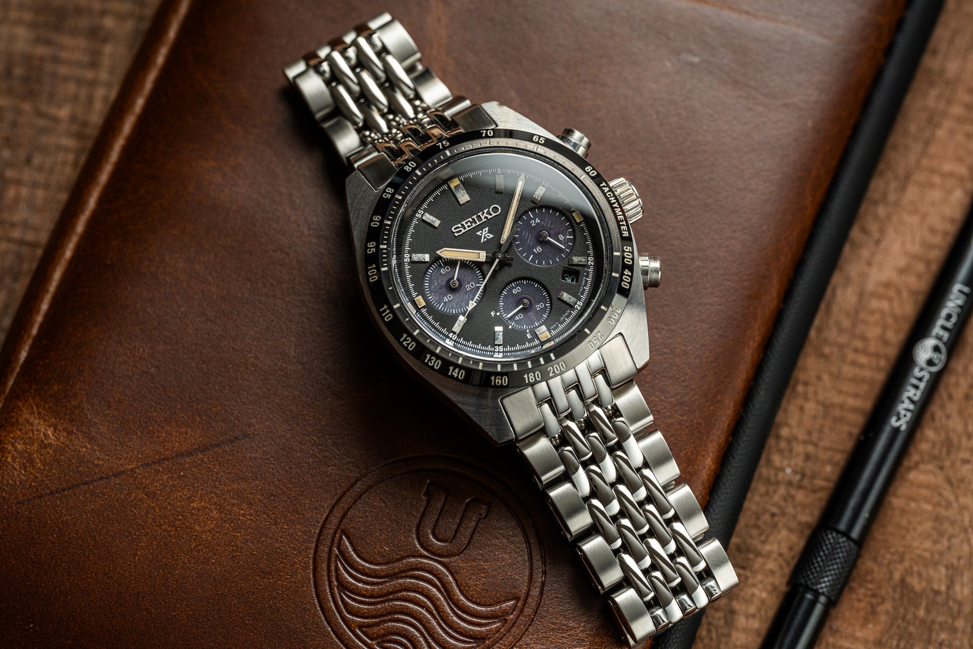 Seiko Speedtimer chronograph watch with black dial, stainless steel bracelet, and tachymeter bezel on brown leather background