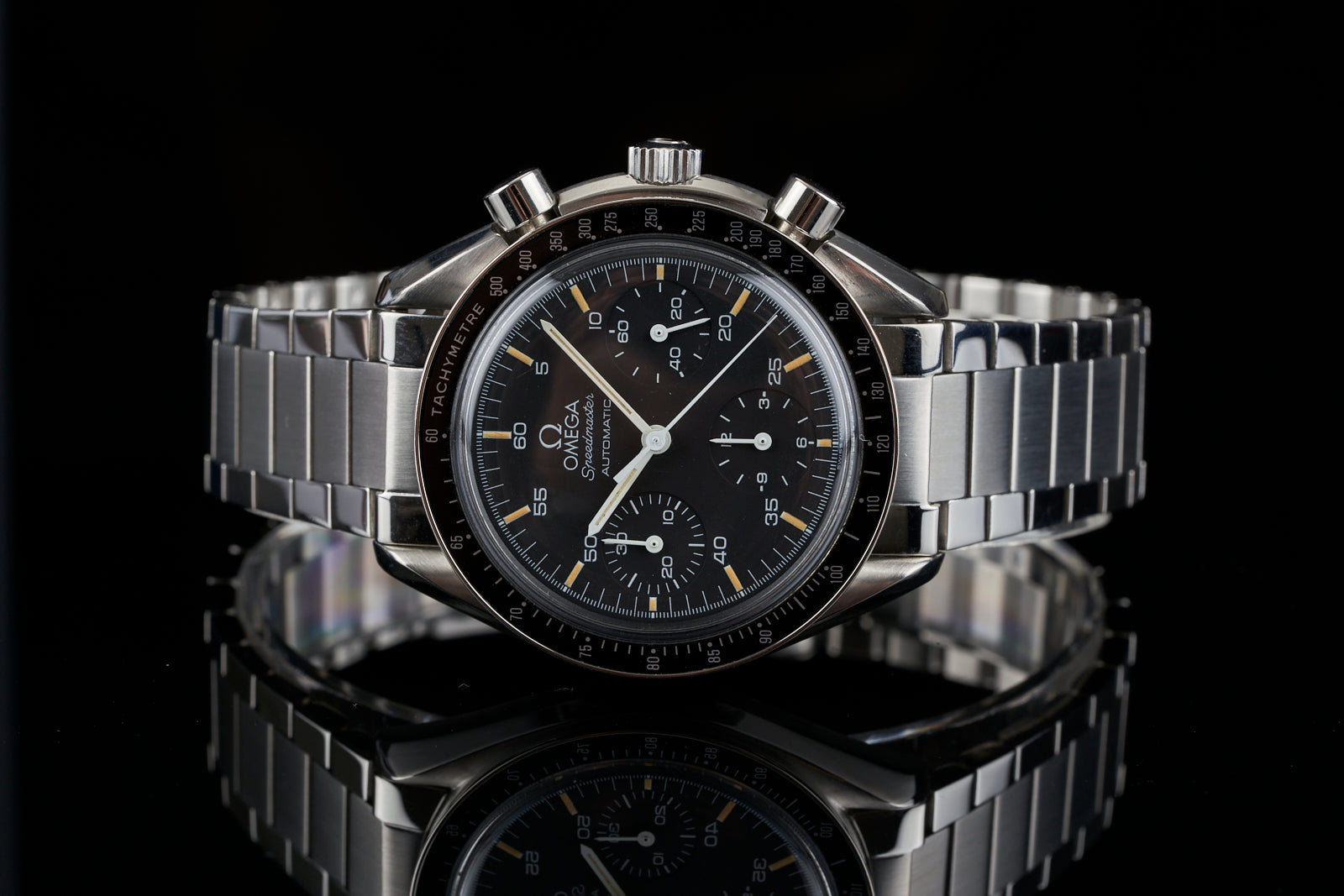 Omega Speedmaster Reduced chronograph watch with black dial, tachymeter bezel, steel bracelet and flat link band on black background