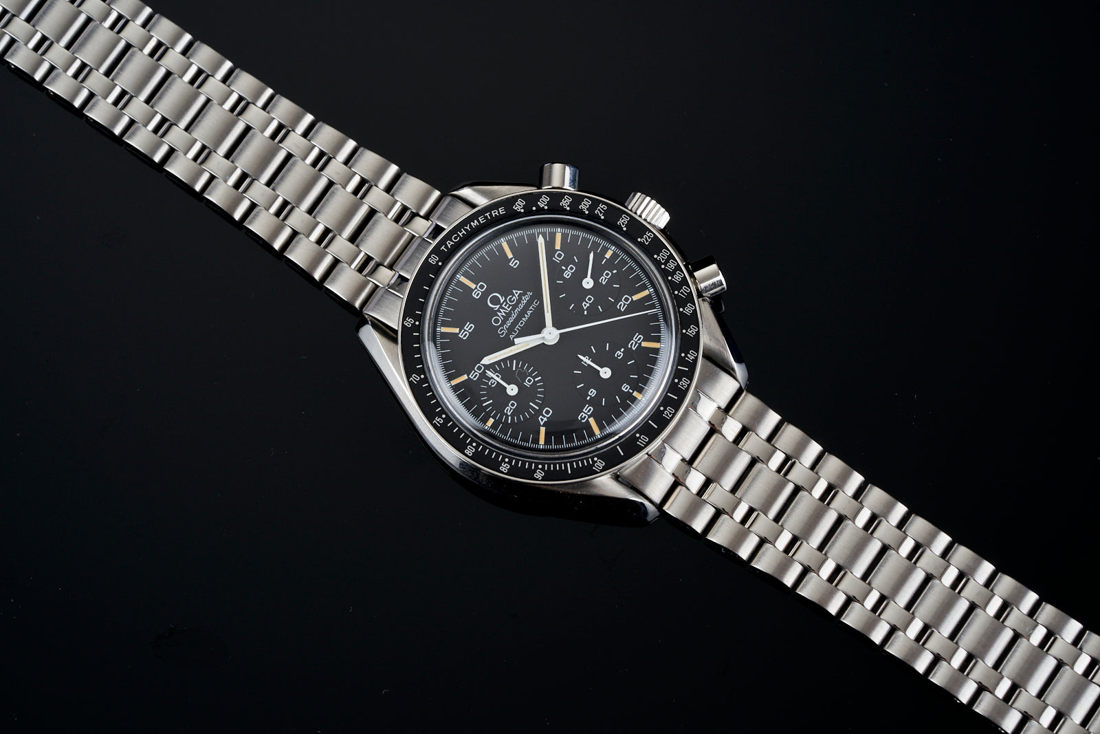 Omega Speedmaster Reduced chronograph watch with black dial, tachymeter bezel, and stainless steel bracelet on black background