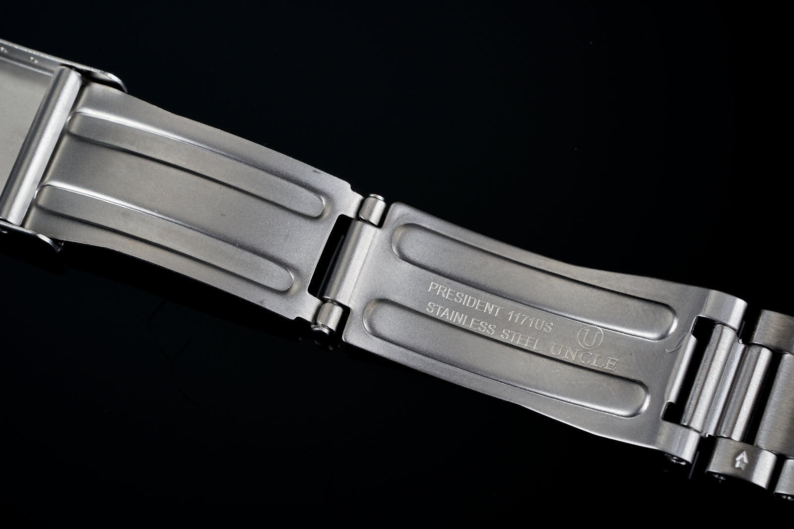 Stainless steel watch bracelet with President 117US engraved links and polished finish against black background