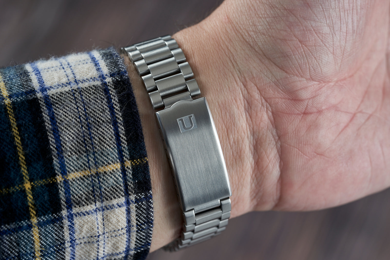 Stainless steel link bracelet with brushed finish and engraved clasp worn on wrist with plaid sleeve