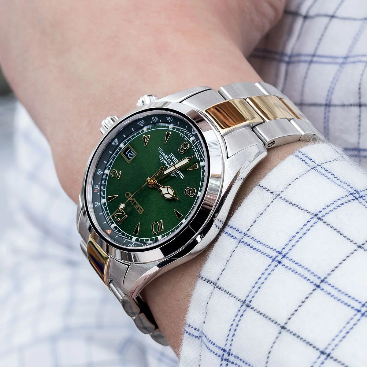 Two-tone silver and gold stainless steel bracelet on green dial luxury watch with tachymeter bezel worn on wrist